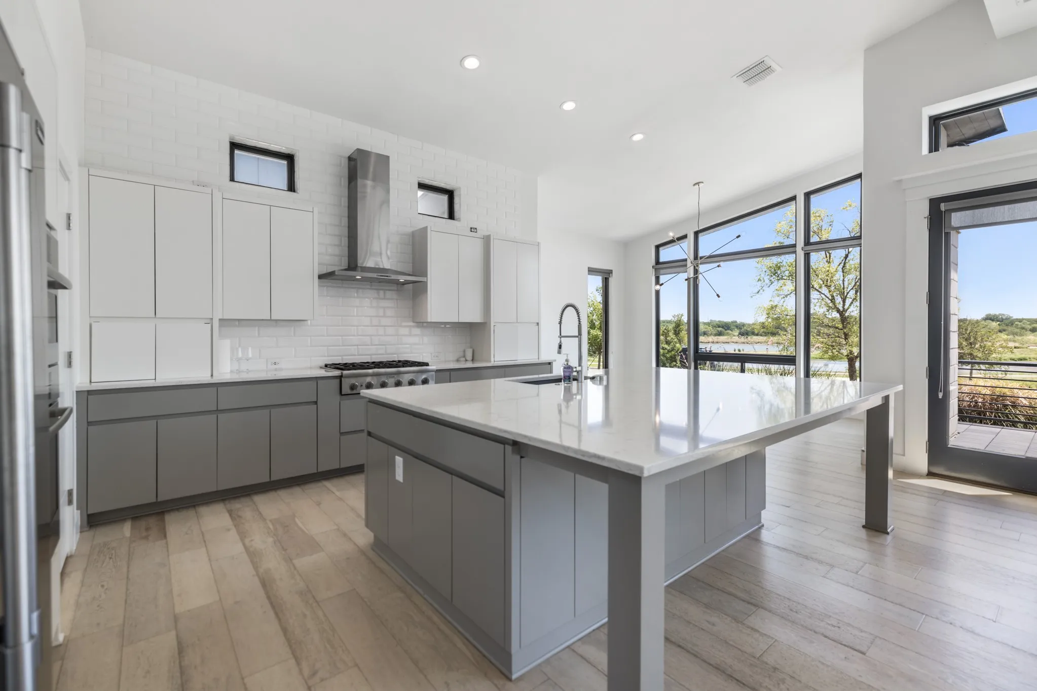 Modern kitchen featuring a large central island with a solid surface countertop, two-tone cabinetry, wood-finish flooring, and a stainless steel range hood