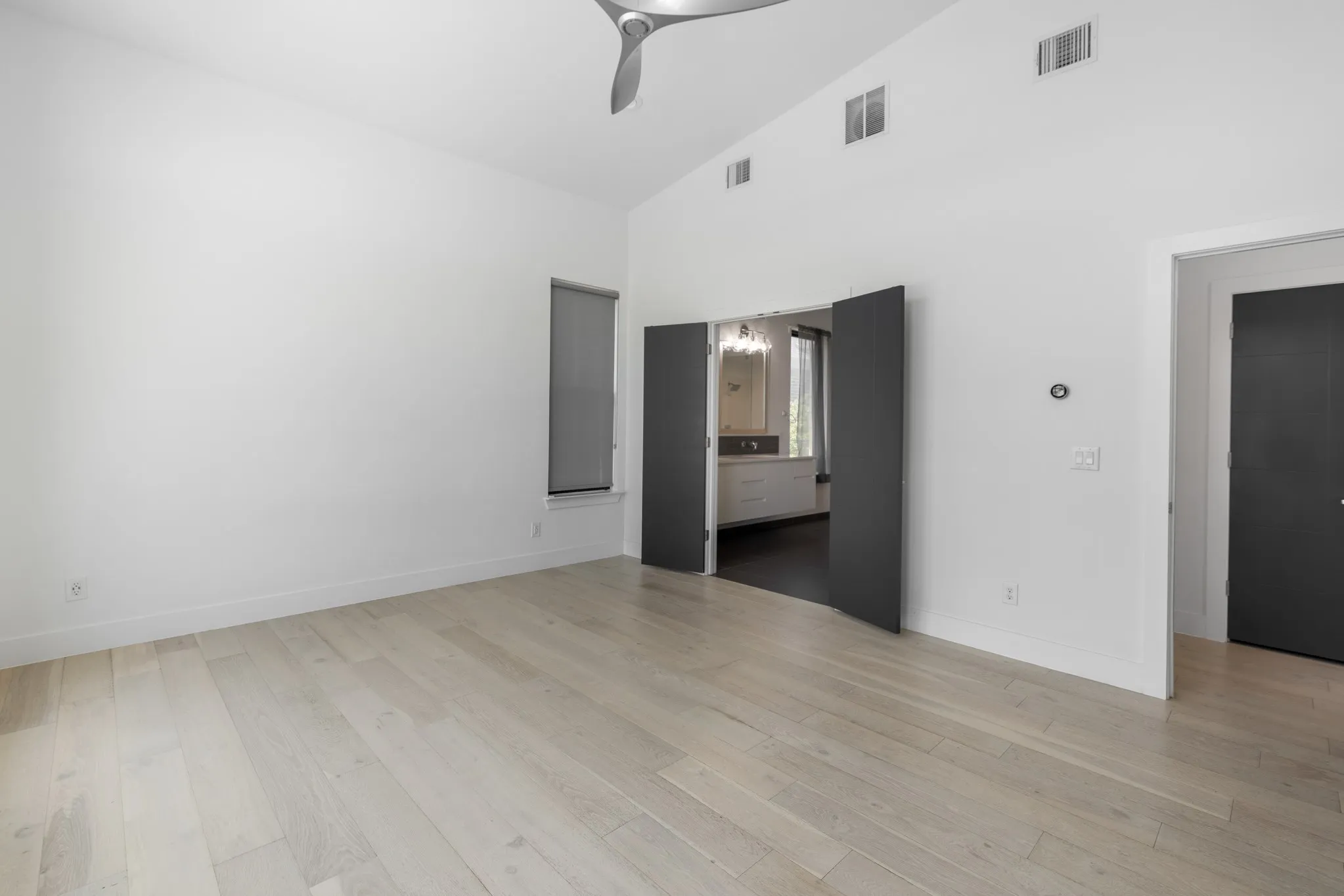 Spacious primary living area featuring wide-plank wood-finish flooring, soaring ceilings with ceiling fan, and multiple entry points