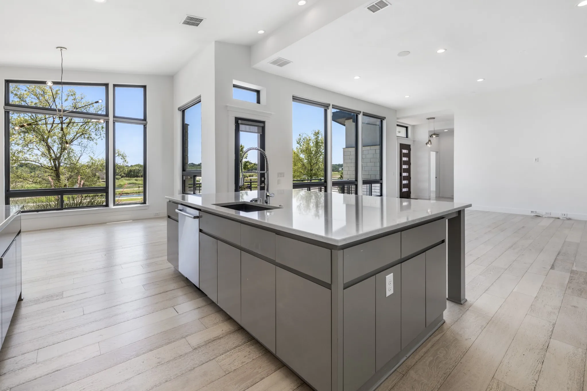 Kitchen island featuring a single basin sink, pull-down faucet, integrated dishwasher, and light-toned countertop