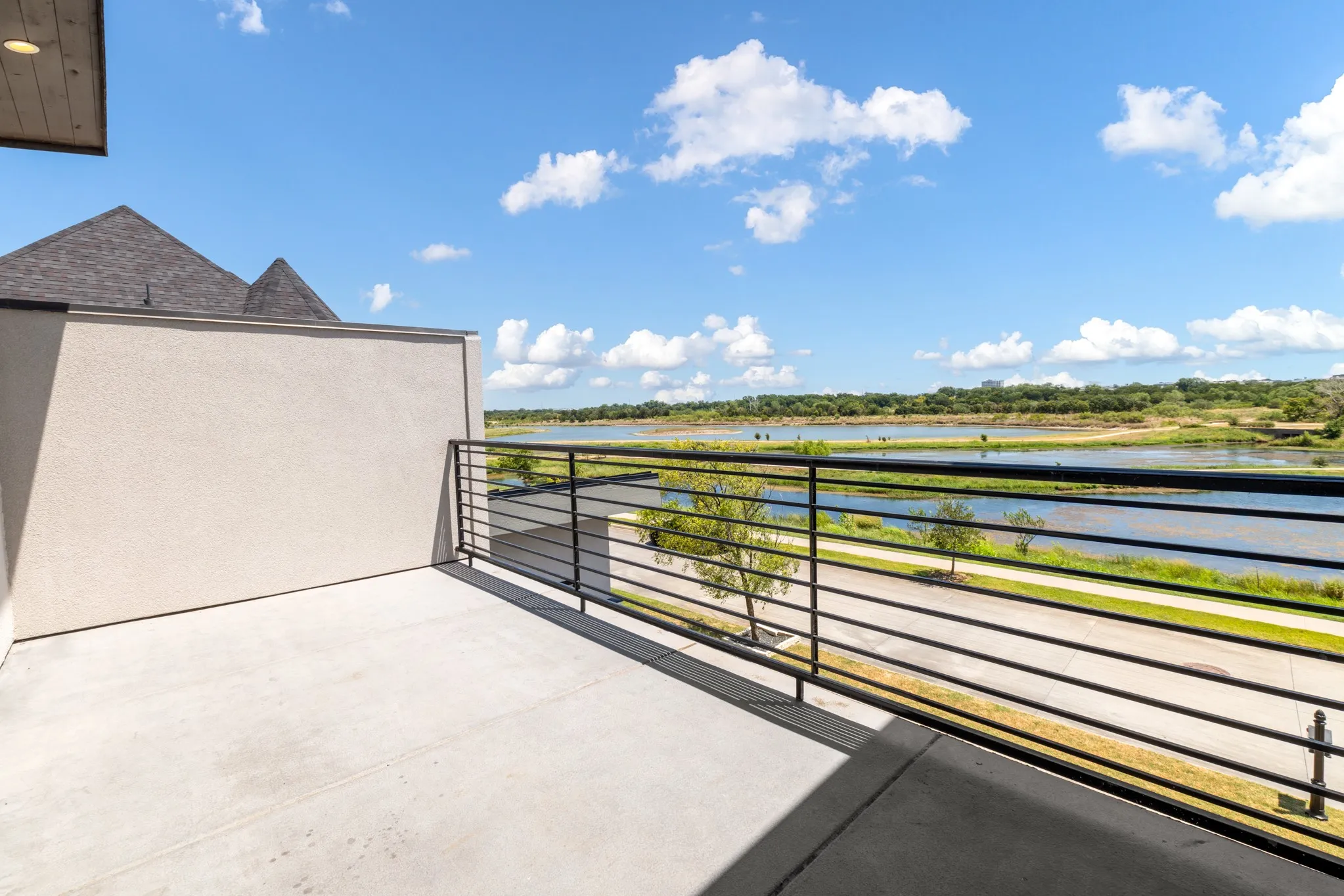 Expansive second-story balcony with horizontal metal railing, concrete decking, and panoramic vistas of manicured grounds and waterfront landscape
