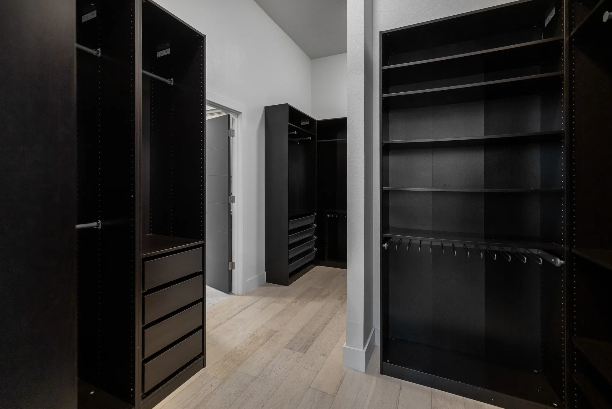 Spacious walk-in closet featuring floor-to-ceiling black cabinetry with multiple shelving sections, integrated drawer storage, and hanging rods for organized wardrobe storage