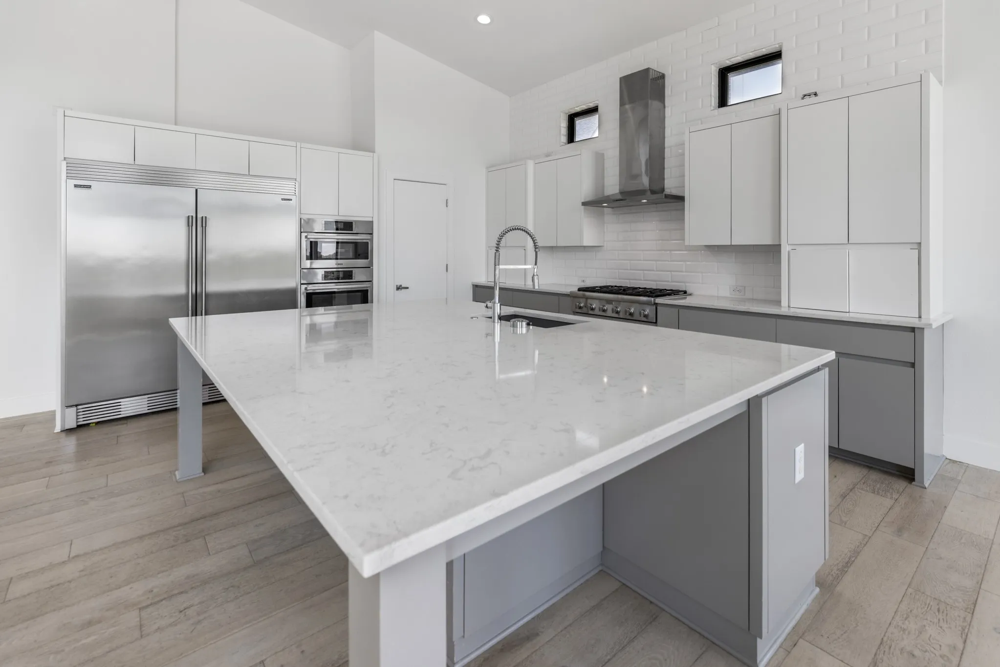 Expansive kitchen island with a light-toned countertop, stainless steel appliances, white cabinetry, and wood-finish flooring