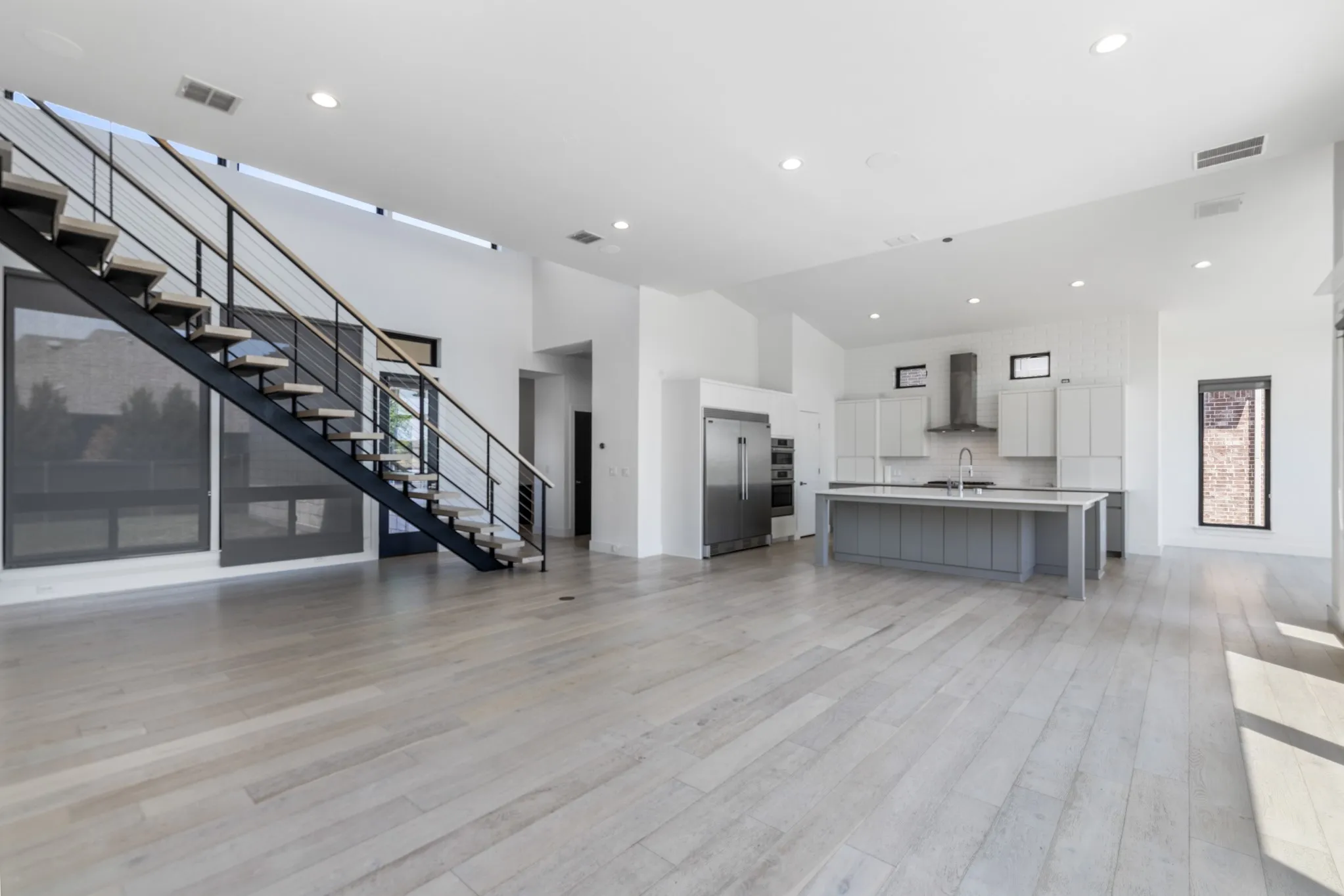 Open-concept living space featuring light wood-finish flooring, recessed ceiling lighting, and floor-to-ceiling windows with metal railings