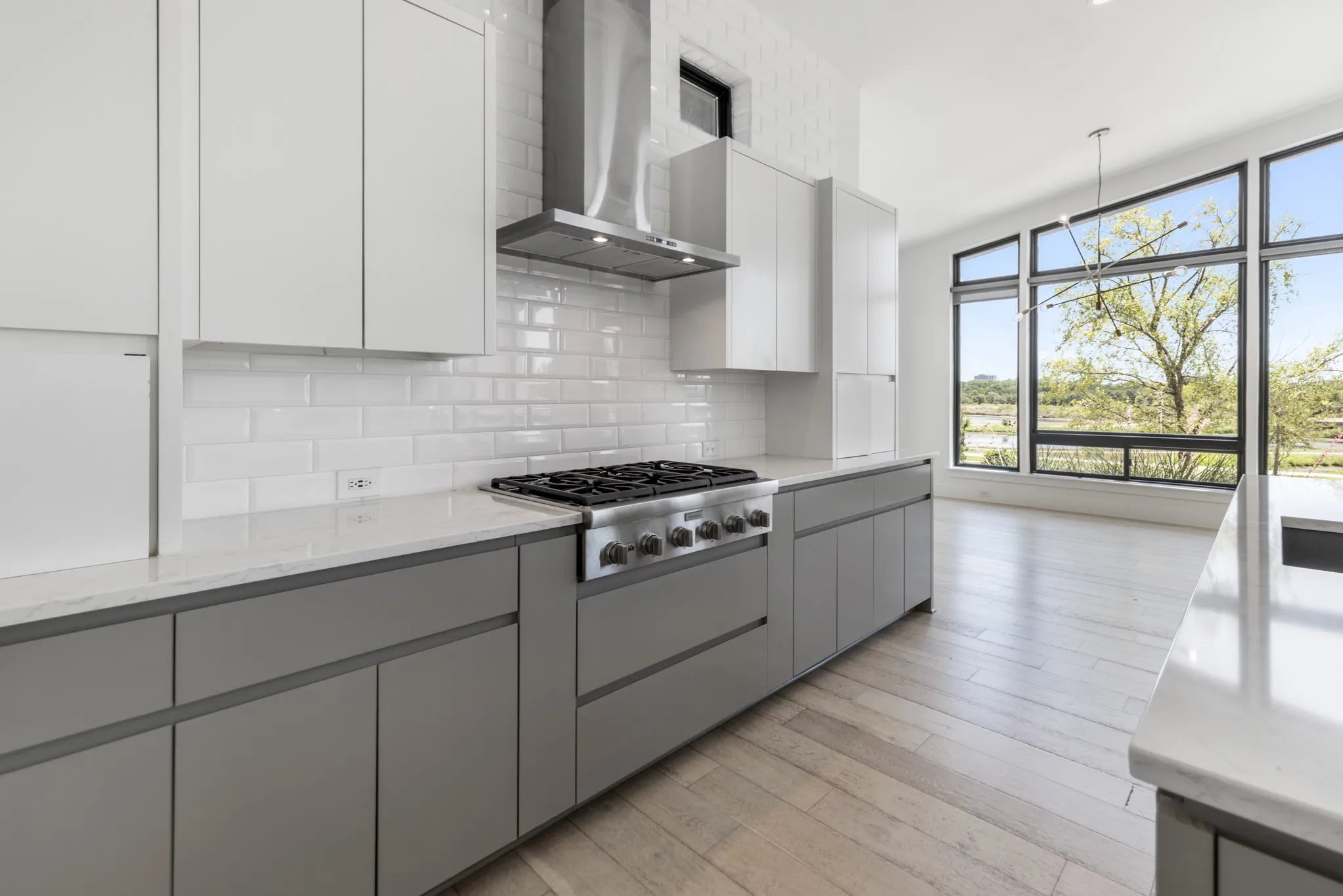 Modern kitchen featuring white cabinetry with gray lower cabinets, stainless steel gas range with overhead hood ventilation, white subway tile backsplash, and wood-finish flooring