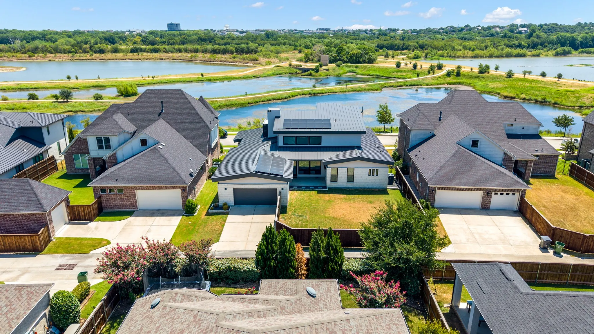 Aerial view showcasing three contemporary brick residences with architectural asphalt shingle roofing, attached garages, and manicured front landscapes