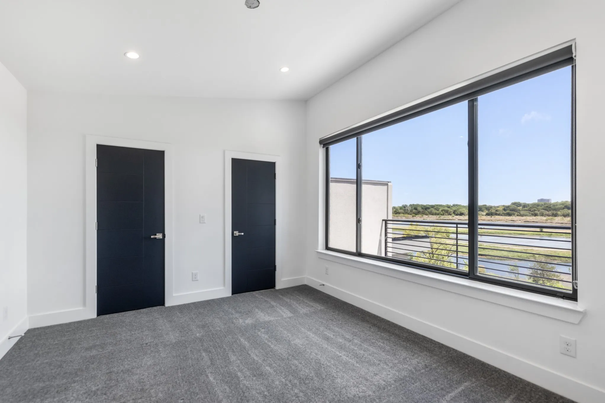 Bright corner bedroom featuring expansive multi-pane windows with black aluminum frames, panoramic countryside outlook, recessed ceiling lighting, neutral wall finishes, and neutral-tone carpeting throughout