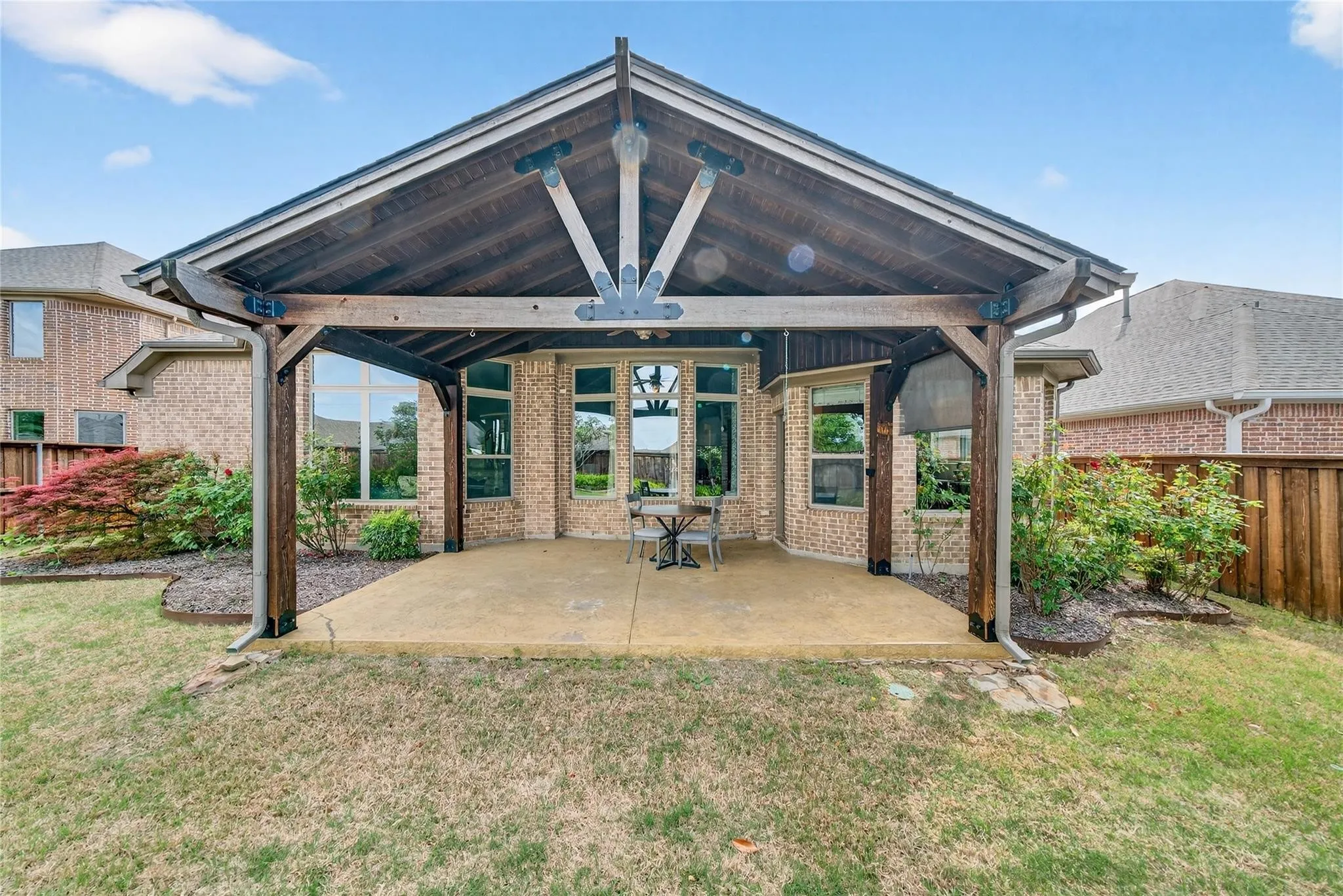 Covered patio with exposed wood beams, concrete flooring, and surrounding brick exterior
