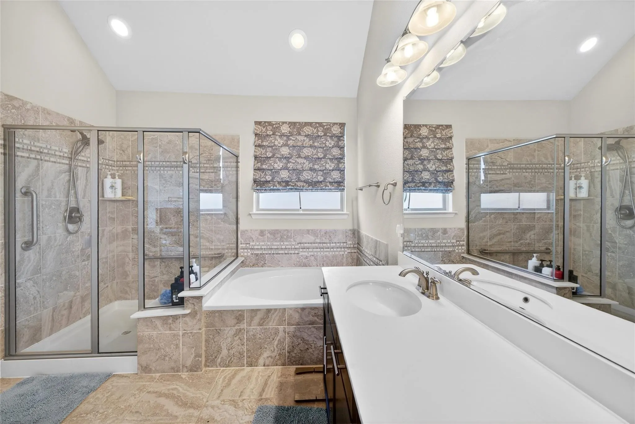 Dual vanity with integrated sinks, a built-in tub, a glass-enclosed shower, and tiled flooring