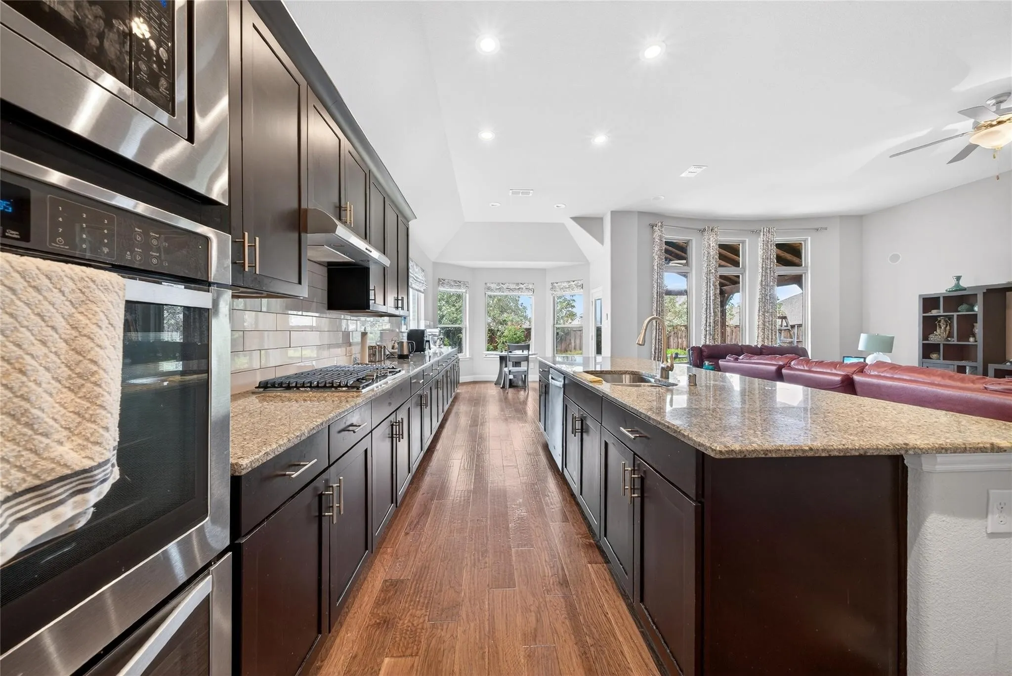 Chef's kitchen featuring stainless steel appliances, dark cabinetry with brushed metal hardware, quartz countertops, subway tile backsplash, and wood-finish flooring throughout