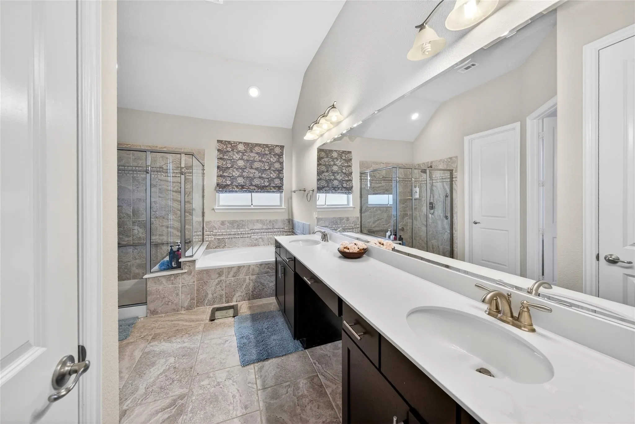 Spa-inspired primary bathroom featuring dual vanities with white quartz countertops, brushed gold faucetry, and an expansive illuminated mirror