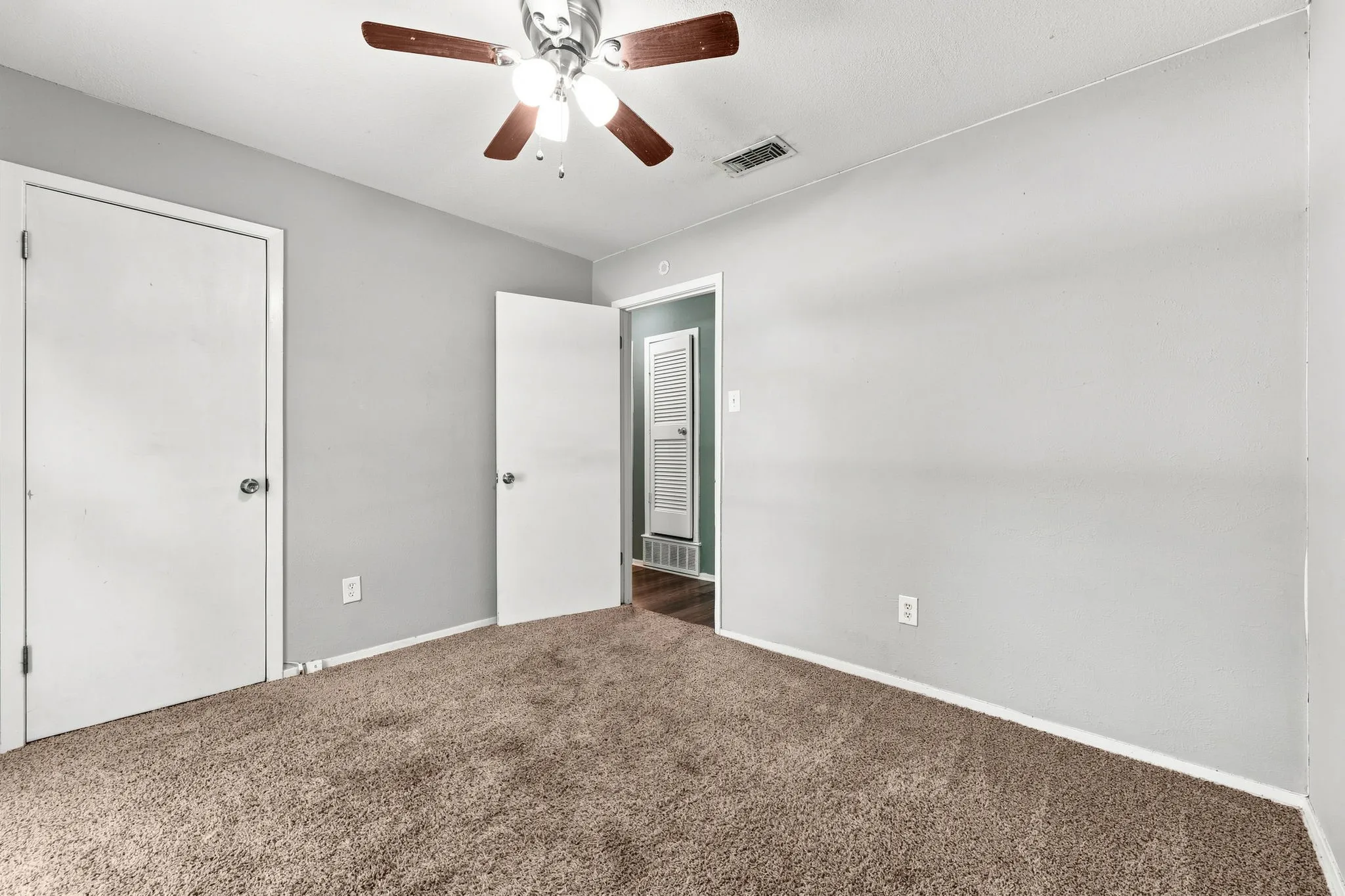 Spacious bedroom with neutral wall finishes, carpeted flooring, ceiling fan with integrated lighting, and multiple closet access points including a mirrored sliding door entry