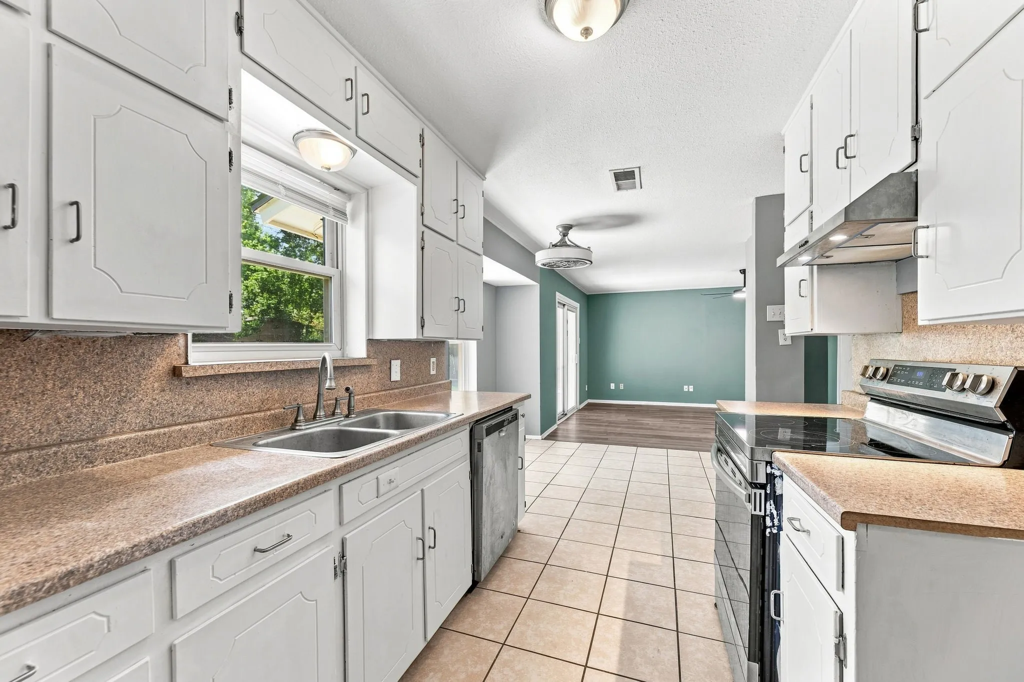 Galley kitchen featuring white cabinetry with brushed nickel hardware, granite countertops, tile flooring, stainless steel appliances including a gas range, and a window overlooking landscaping