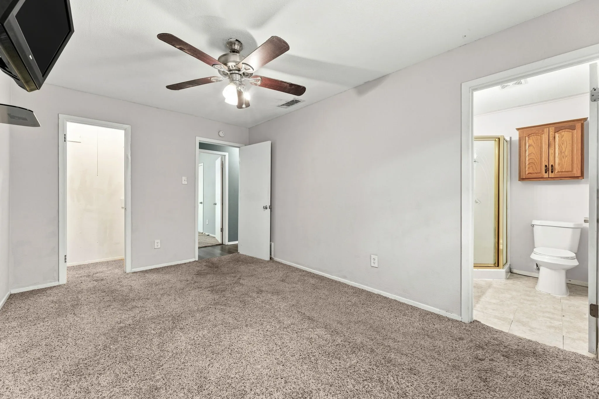 Spacious primary bedroom featuring neutral carpeting, ceiling fan with integrated lighting, and direct access to an ensuite bathroom