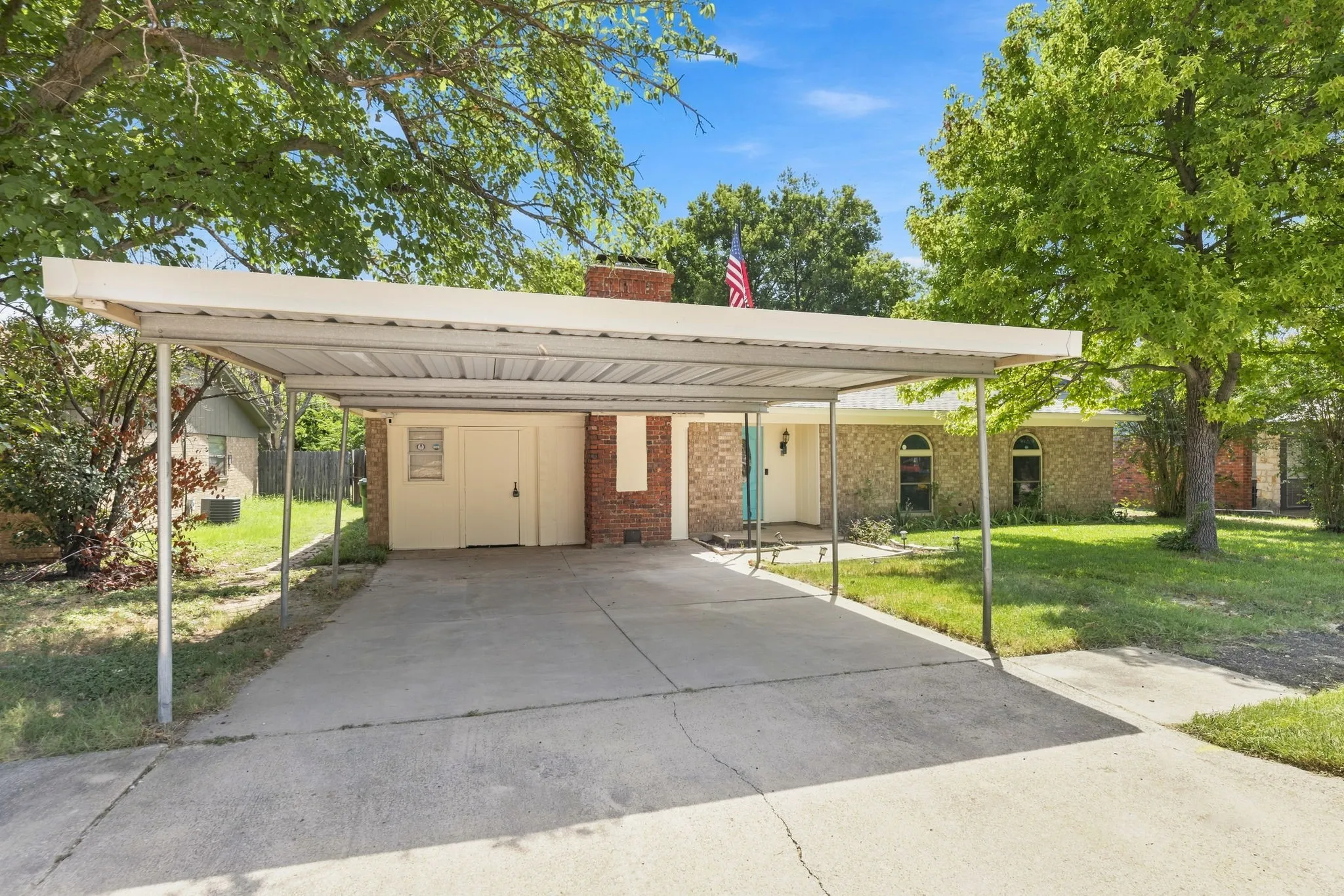 Brick home featuring a covered carport with metal framework and concrete driveway