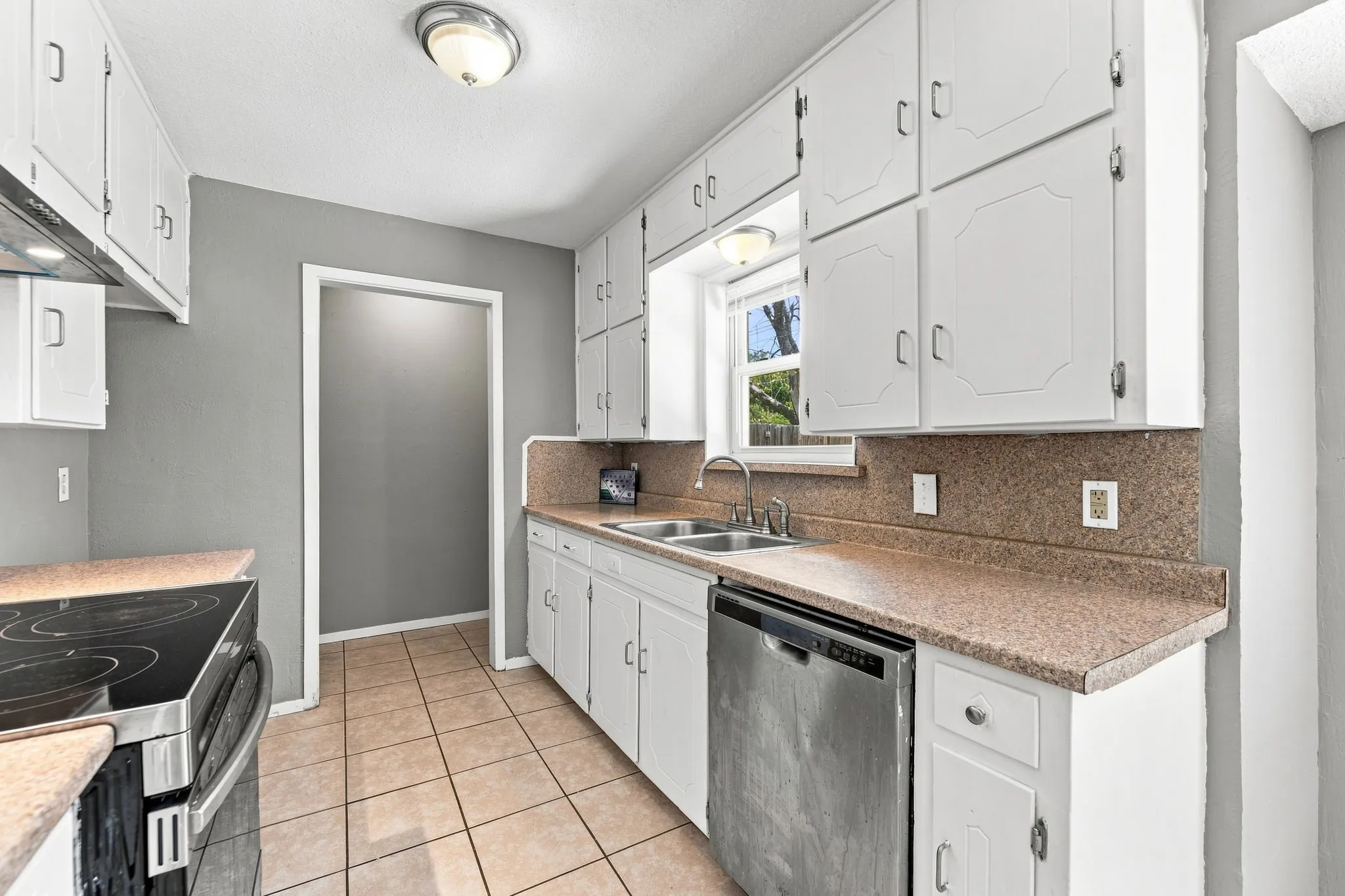 Galley kitchen featuring white cabinetry with hardware accents, quartz-style countertops, tile flooring, and stainless steel appliances including a dishwasher