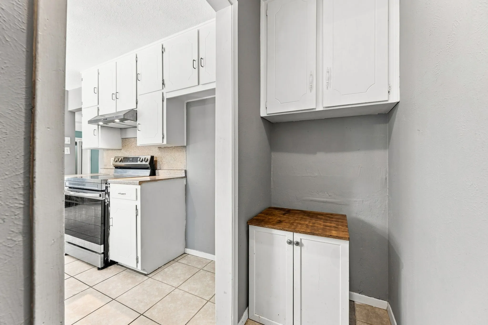 Efficient galley kitchen featuring white cabinetry, stainless steel appliances, tile flooring, and a dedicated pantry with wood-finish countertop and ample storage