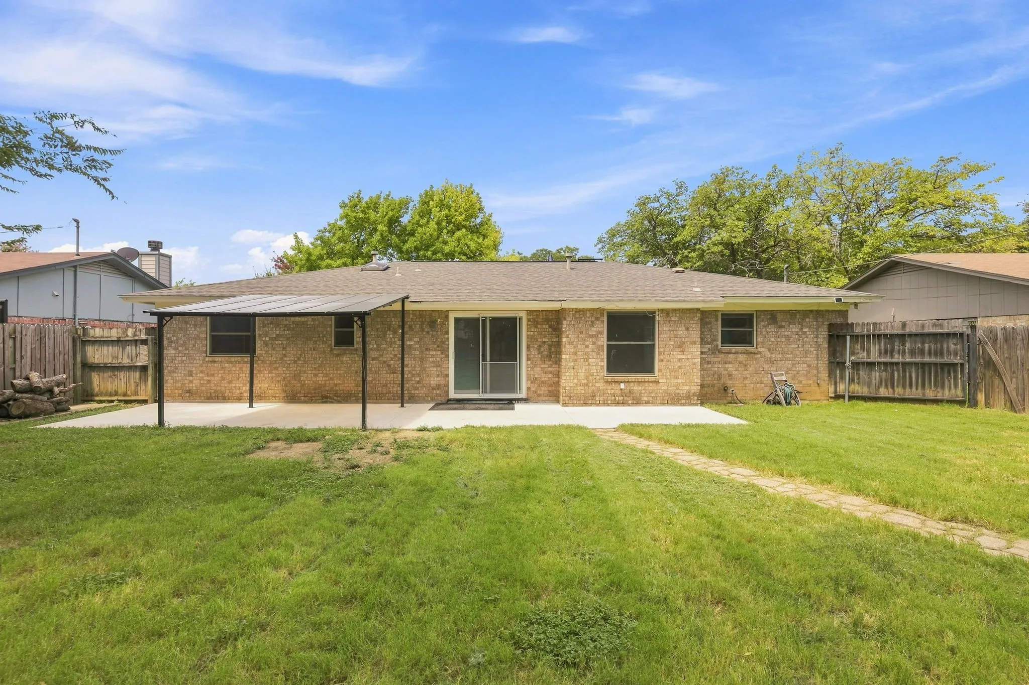 Expansive backyard featuring a brick exterior, covered patio, sliding glass door, multiple windows, and a wood privacy fence