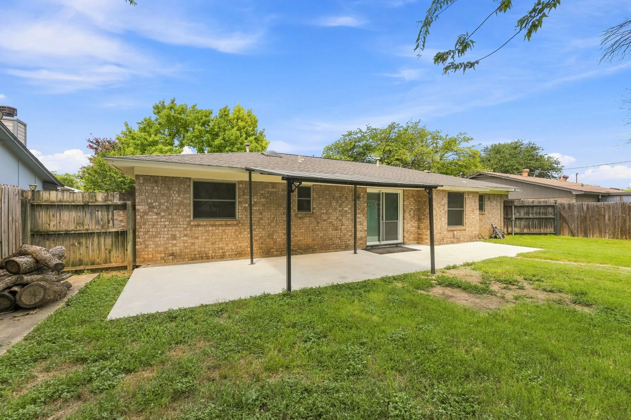 Expansive backyard with a covered patio, brick exterior, sliding glass door, and wooden privacy fencing