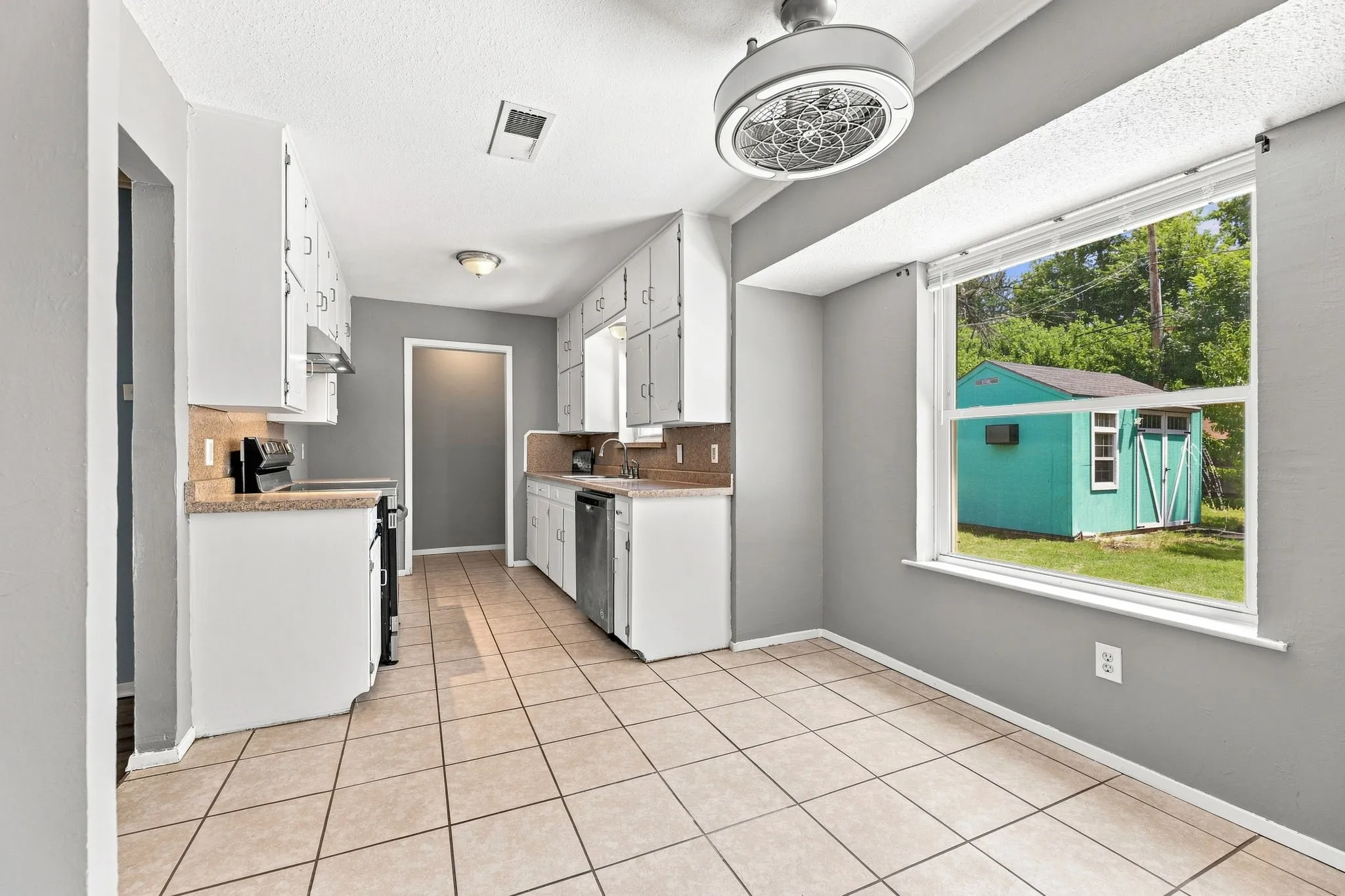 Galley-style kitchen featuring white cabinetry, tile flooring, stainless steel appliances, and ample counter workspace