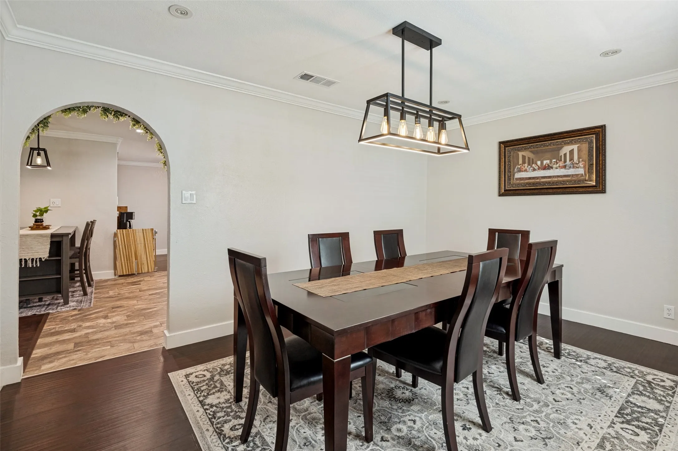 Crown molding, recessed lighting, and a modern linear chandelier illuminate the dining space