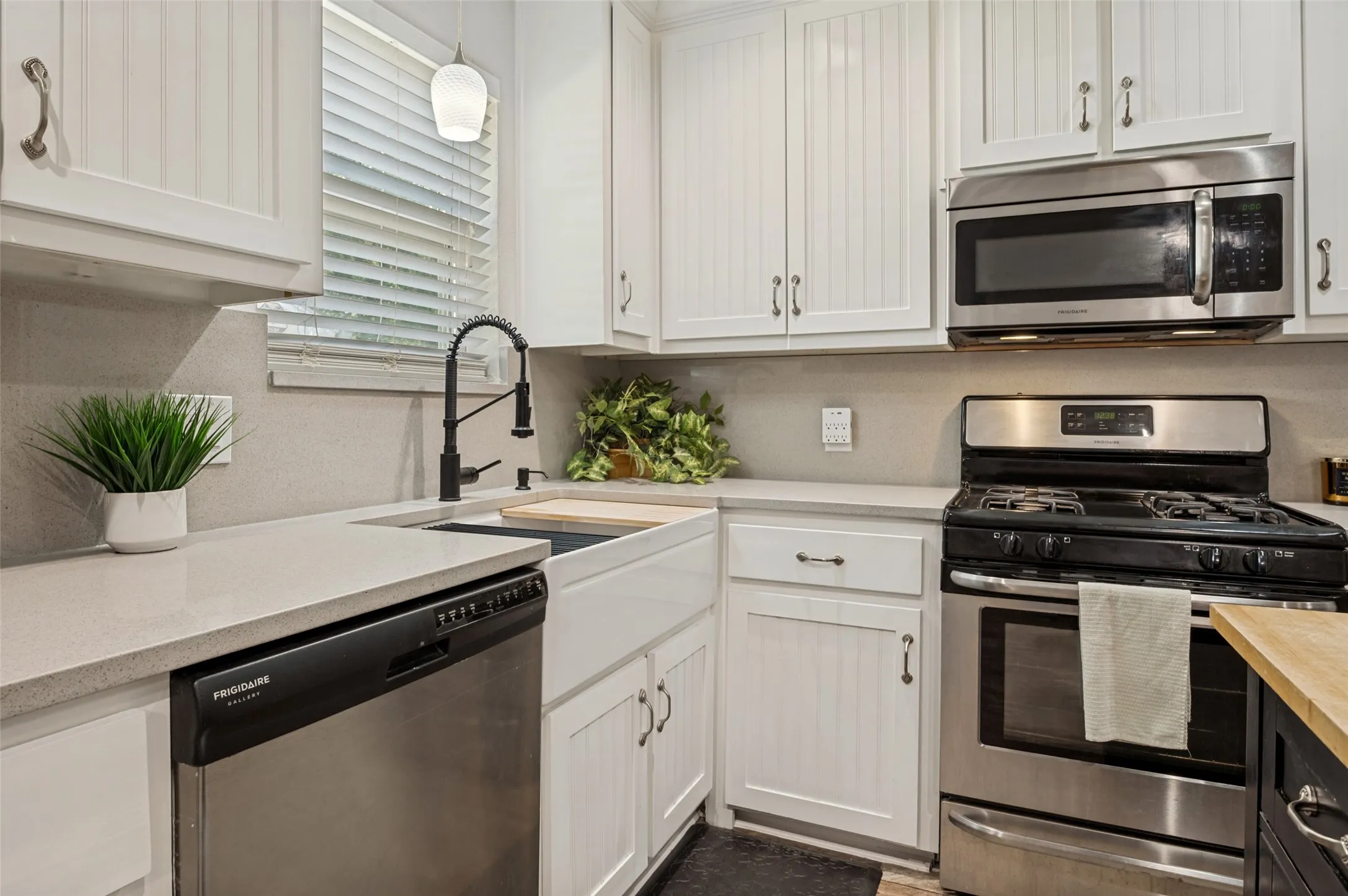 Modern kitchen featuring white shaker cabinetry, stainless steel appliances including a gas range and microwave hood combination, quartz countertops, a deep farmhouse sink with matte black pull-down faucet, and subway tile backsplash accents