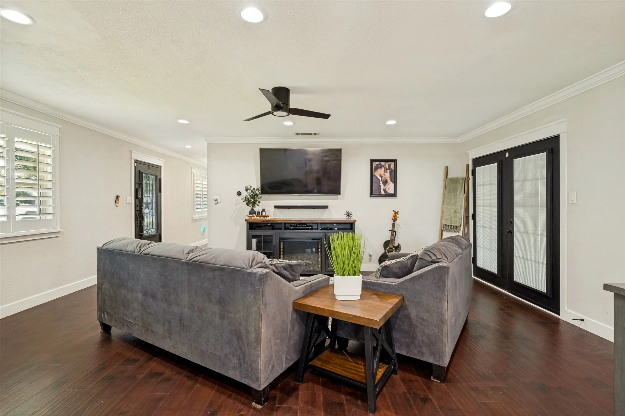 Spacious living room featuring dark wood flooring, a ceiling fan with recessed lighting, and a wall-mounted flat-screen TV above a fireplace with a dark surround