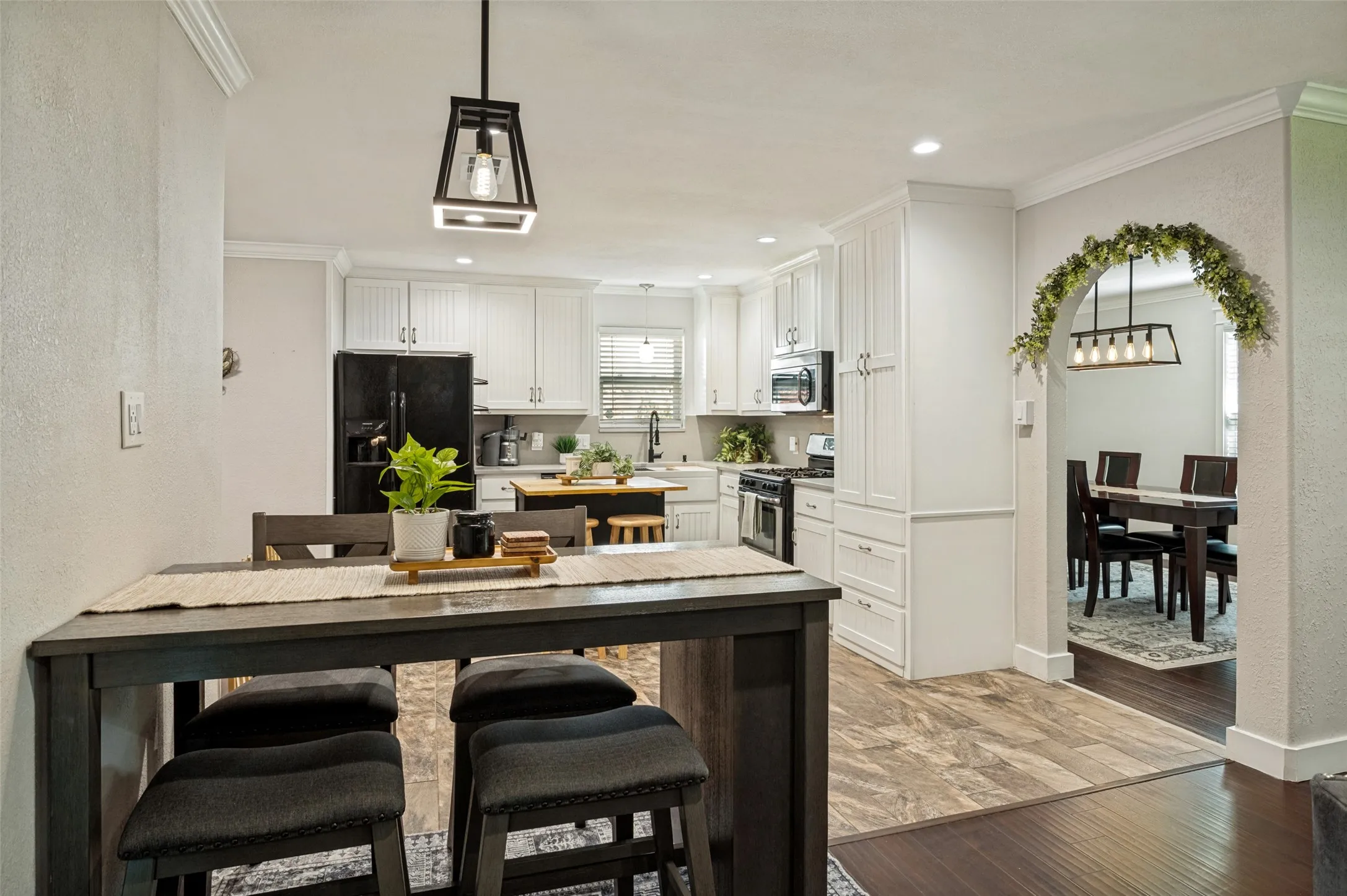 Open-concept kitchen and dining area featuring white cabinetry, stainless steel appliances, wood-finish flooring, a dark wood island with seating, and pendant lighting overhead