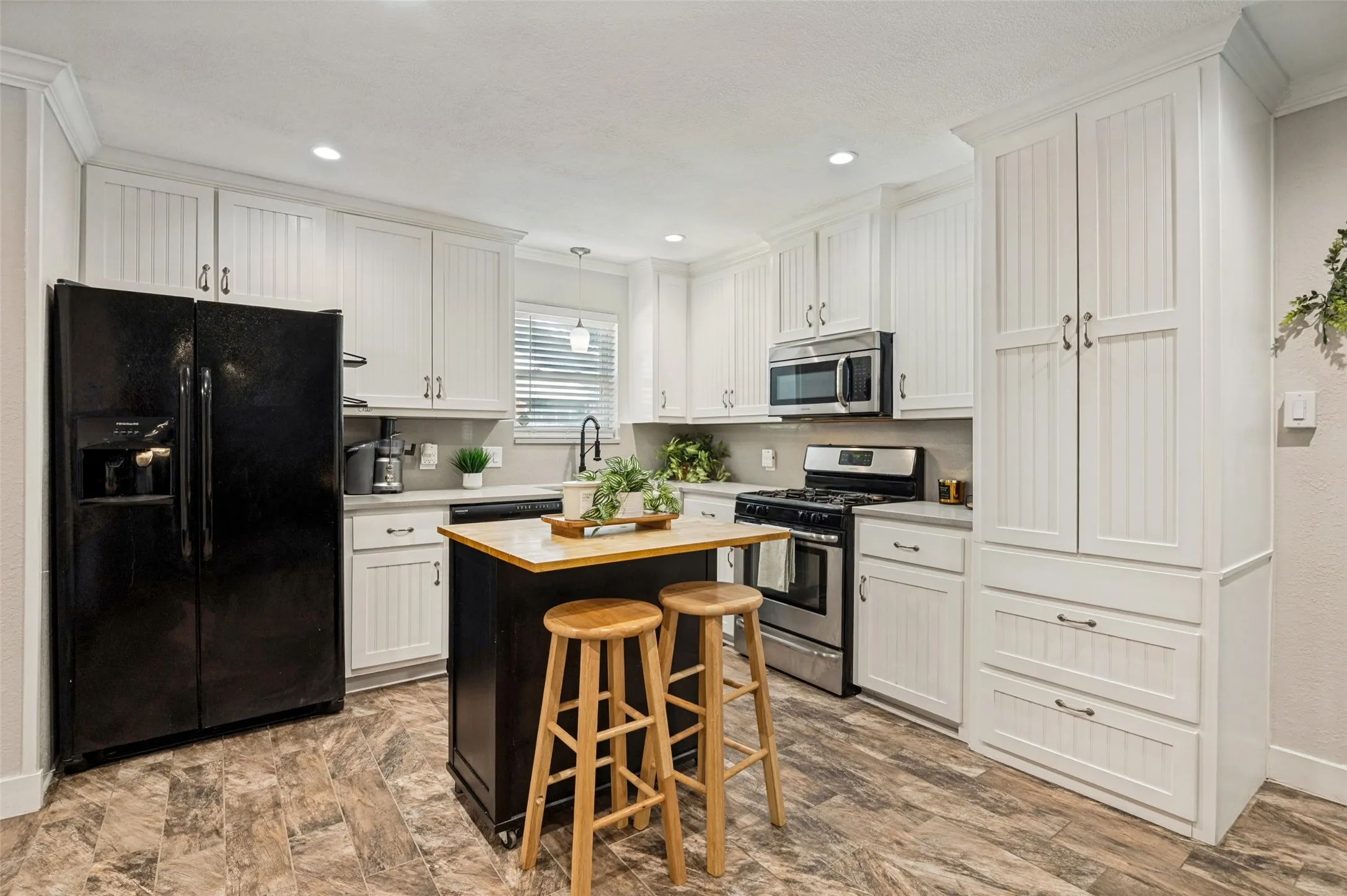 Modern kitchen featuring crisp white cabinetry with chrome hardware, stainless steel appliances including a built-in wall oven, and a contrasting black island with butcher-block countertop and seating for two