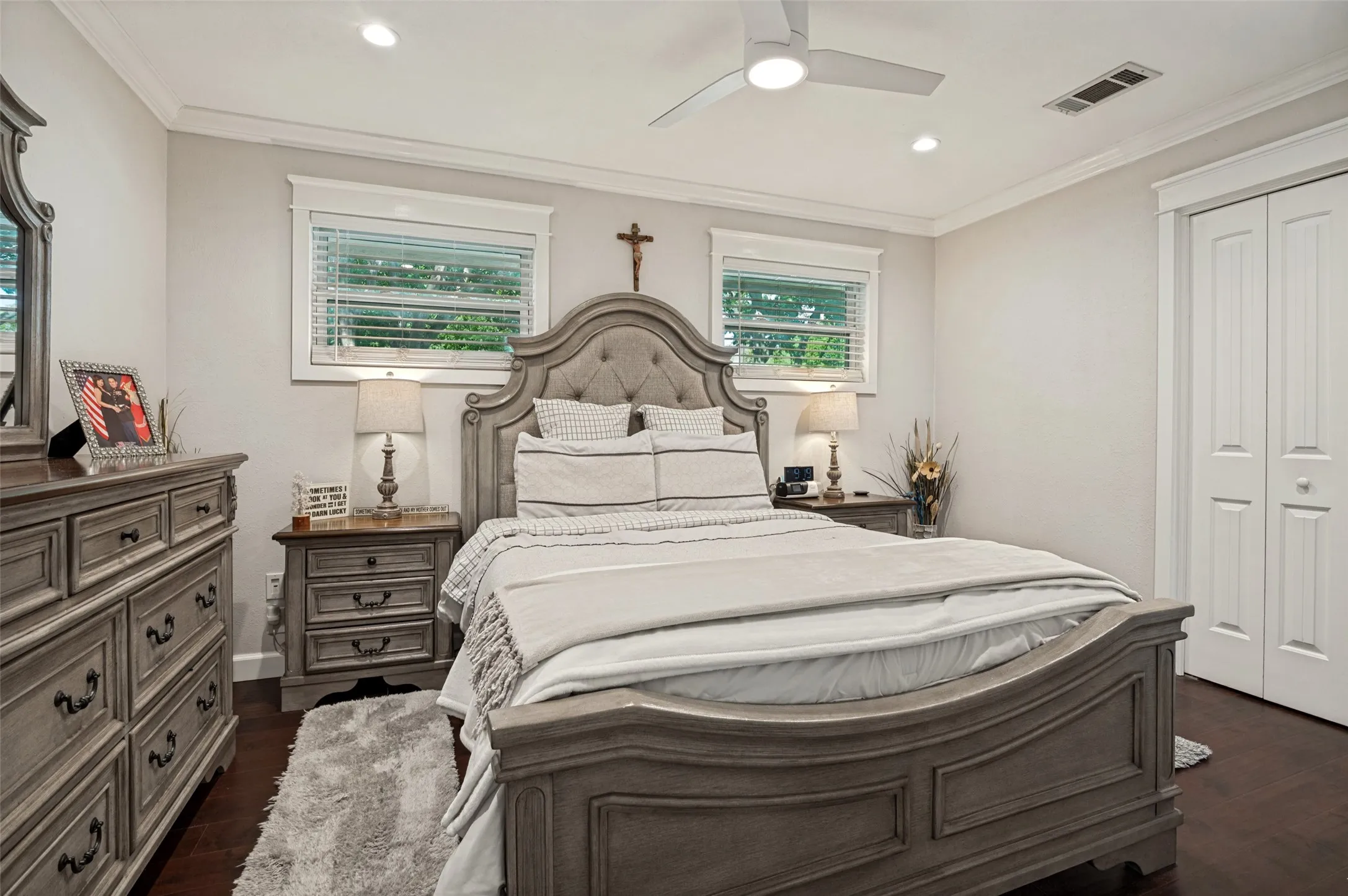 Elegant primary bedroom showcasing a curved-top upholstered headboard, dual nightstands with decorative hardware, recessed ceiling lighting, and a ceiling fan