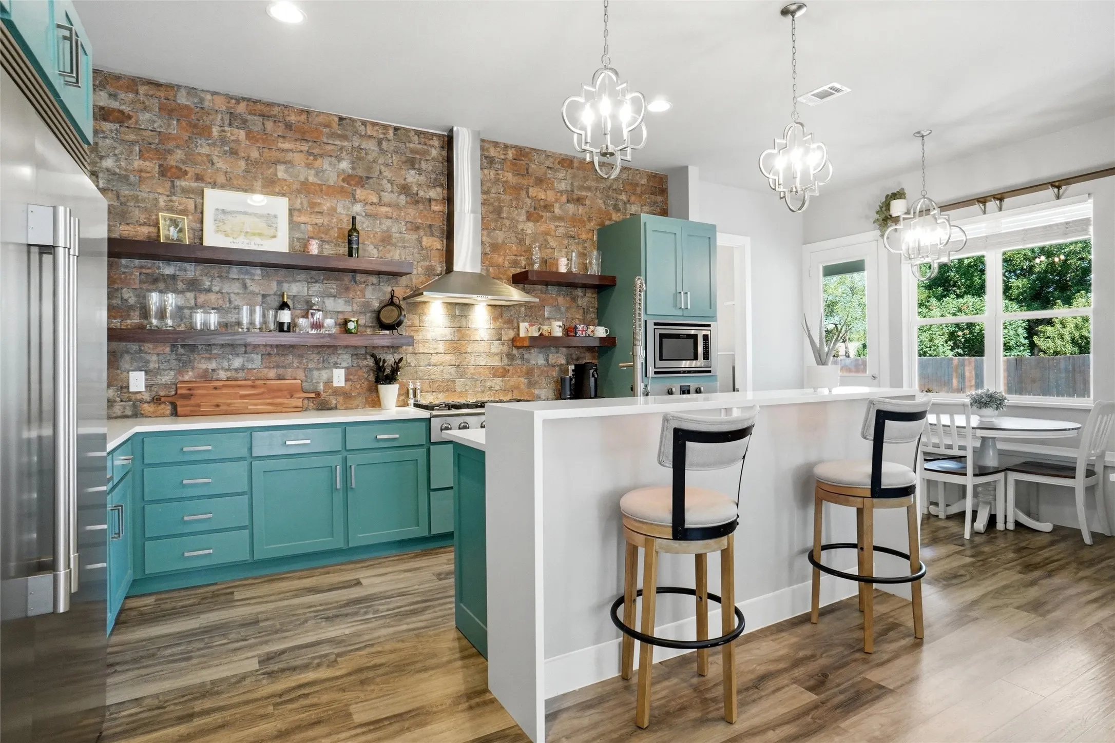 This is a beautiful country kitchen! The island breakfast bar is topped with white quartz and from the barstools you overlook the breakfast area and rear yard. The back wall is brick with floating shelving.