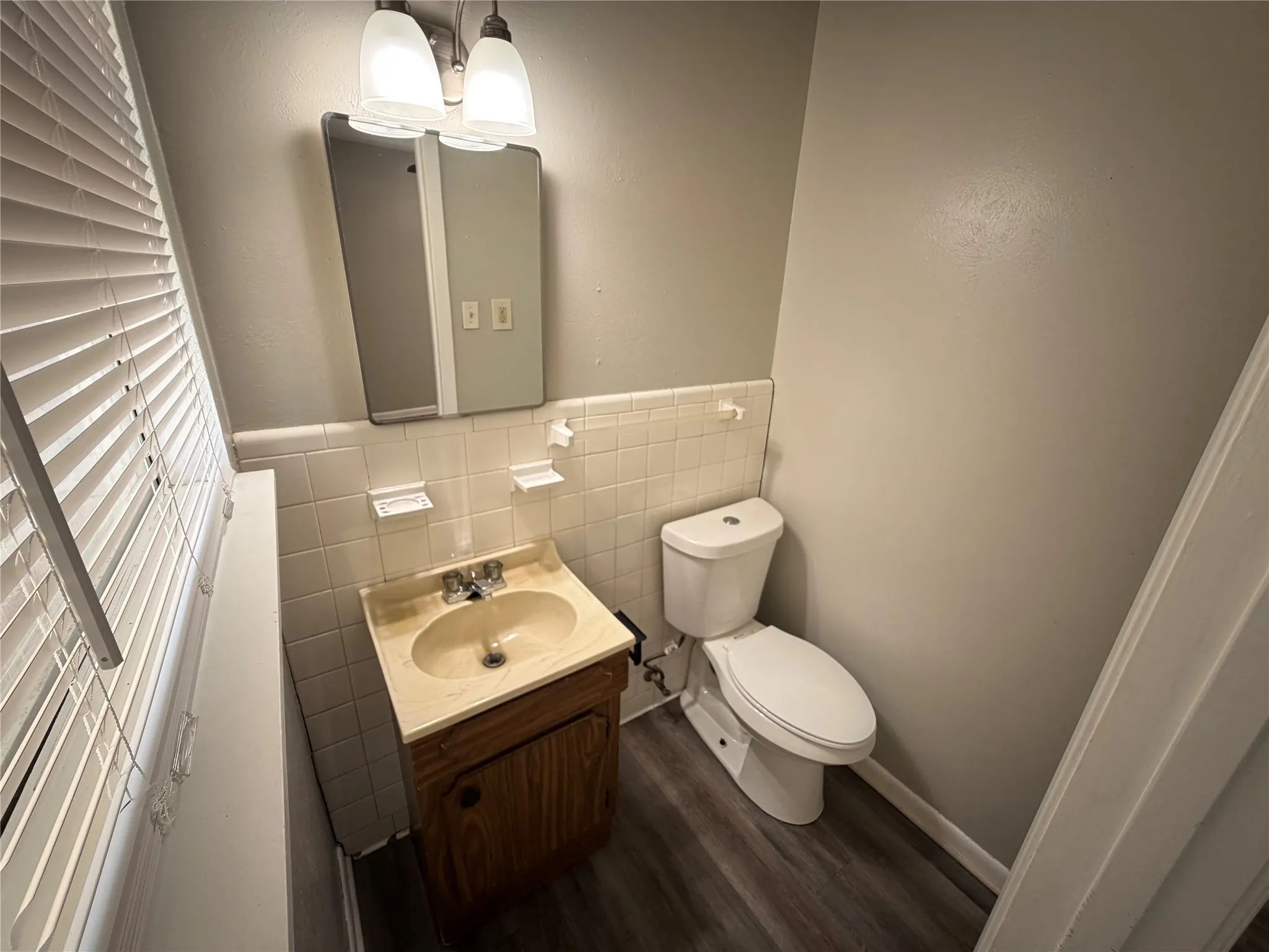 Wood-finish flooring, white wall tiling, a vanity with integrated sink, and a wall-mounted mirror