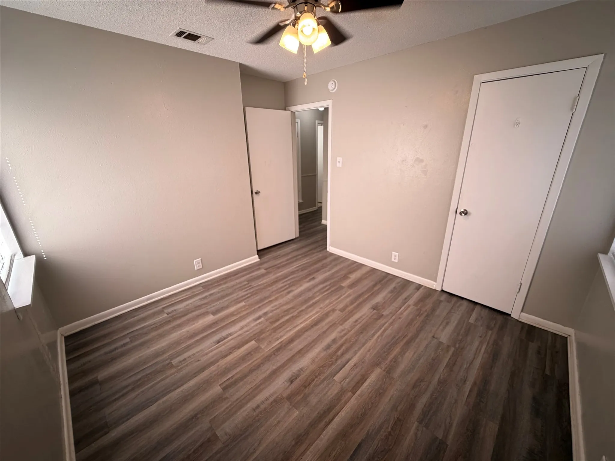 Spacious bedroom featuring wood-finish flooring, neutral wall finishes, ceiling fan with integrated lighting, and multiple closet doors providing ample storage