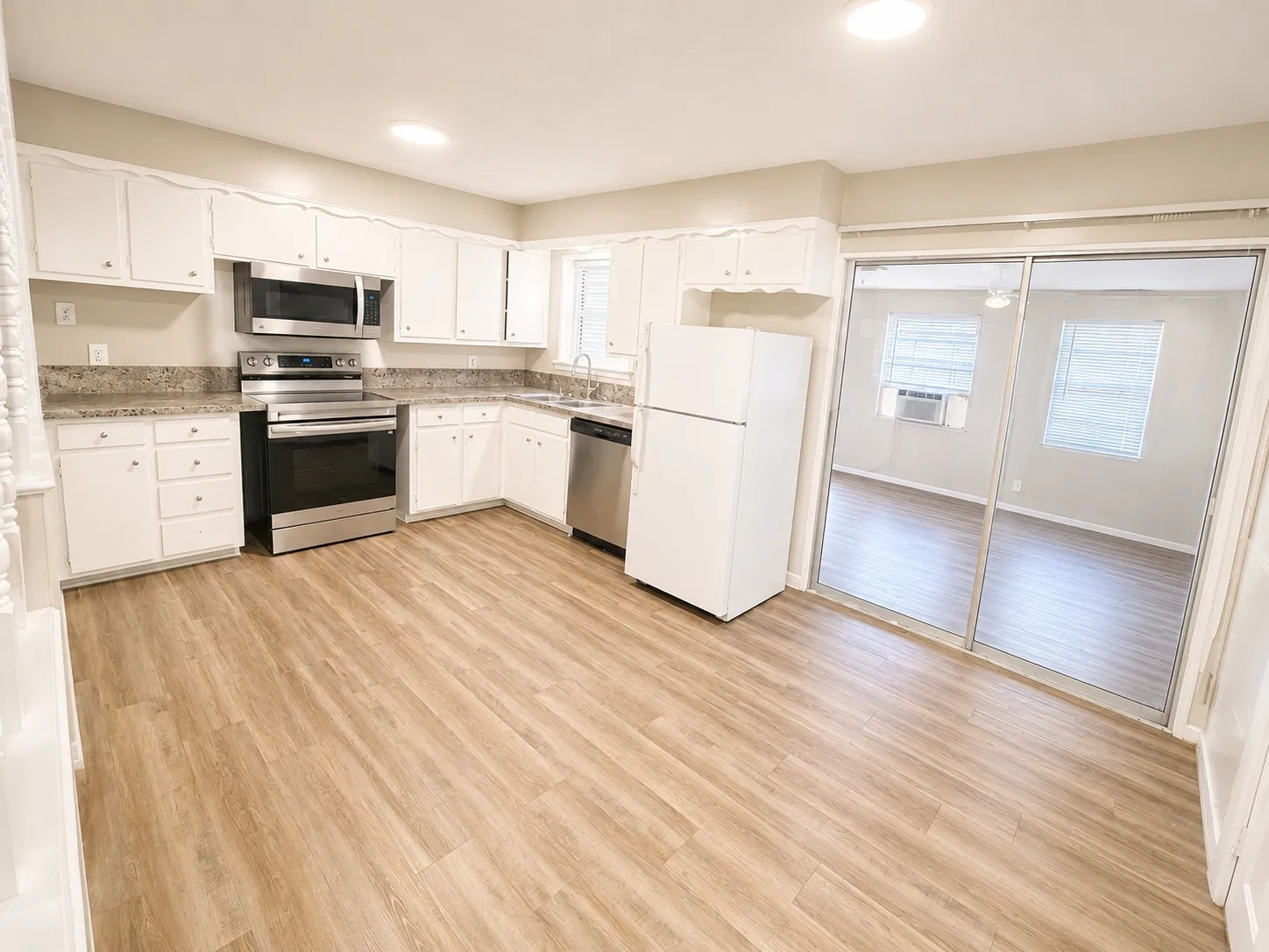 Spacious kitchen featuring white cabinetry, stainless steel appliances including a microwave and electric range, tile backsplash, and wood-finish flooring
