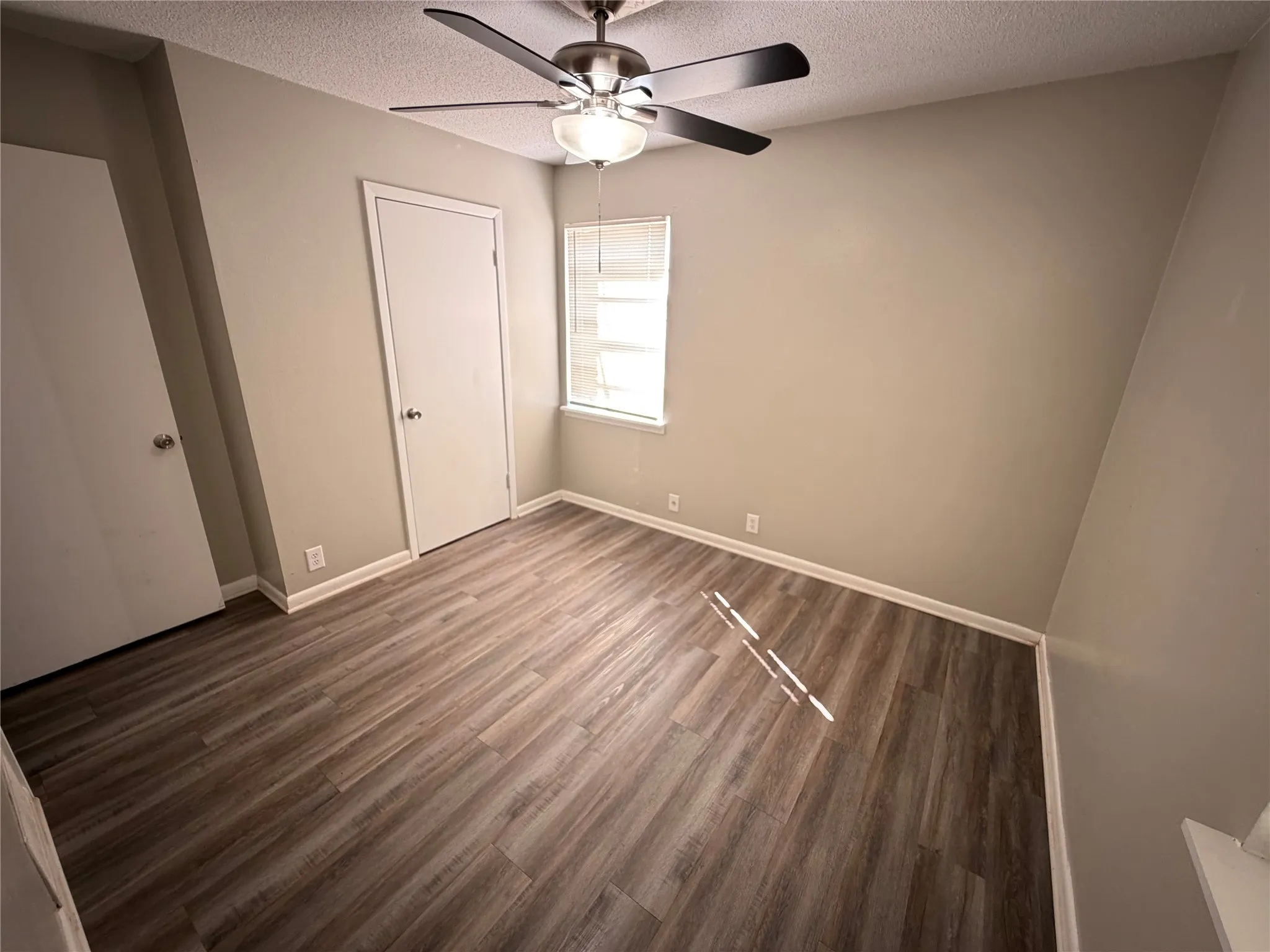 Wood-finish flooring, neutral wall tones, window with horizontal blinds, ceiling fan with integrated lighting, and white trim