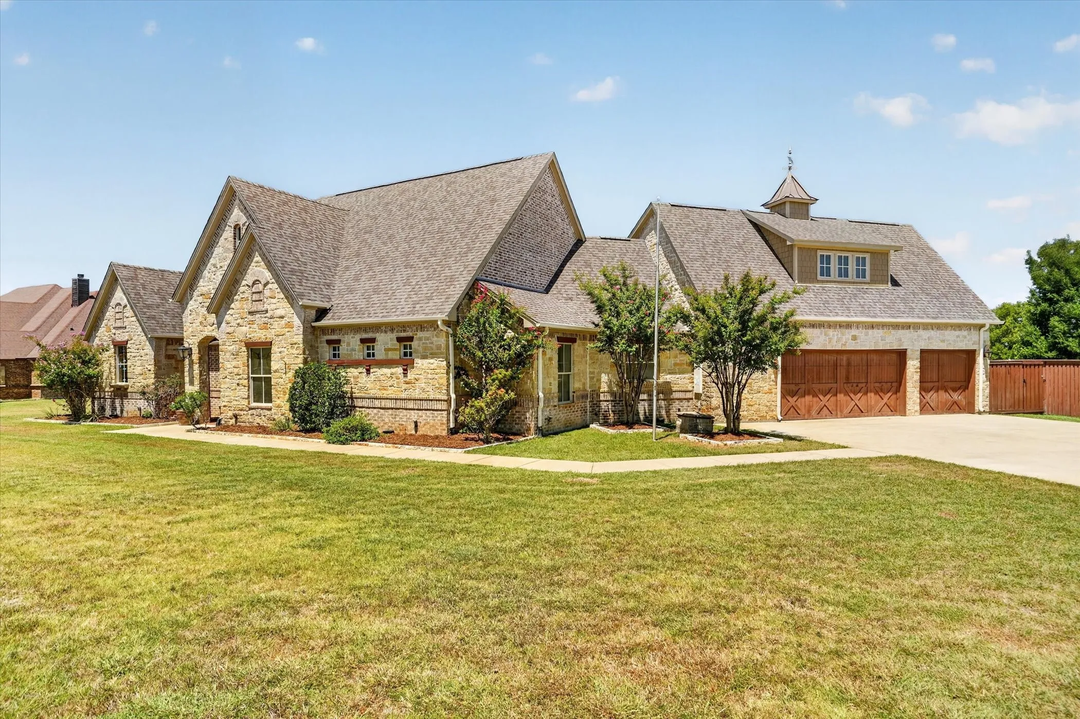 Stone exterior with a shingled roof, a three-car garage with wood-finish doors, and a dormer with a cupola