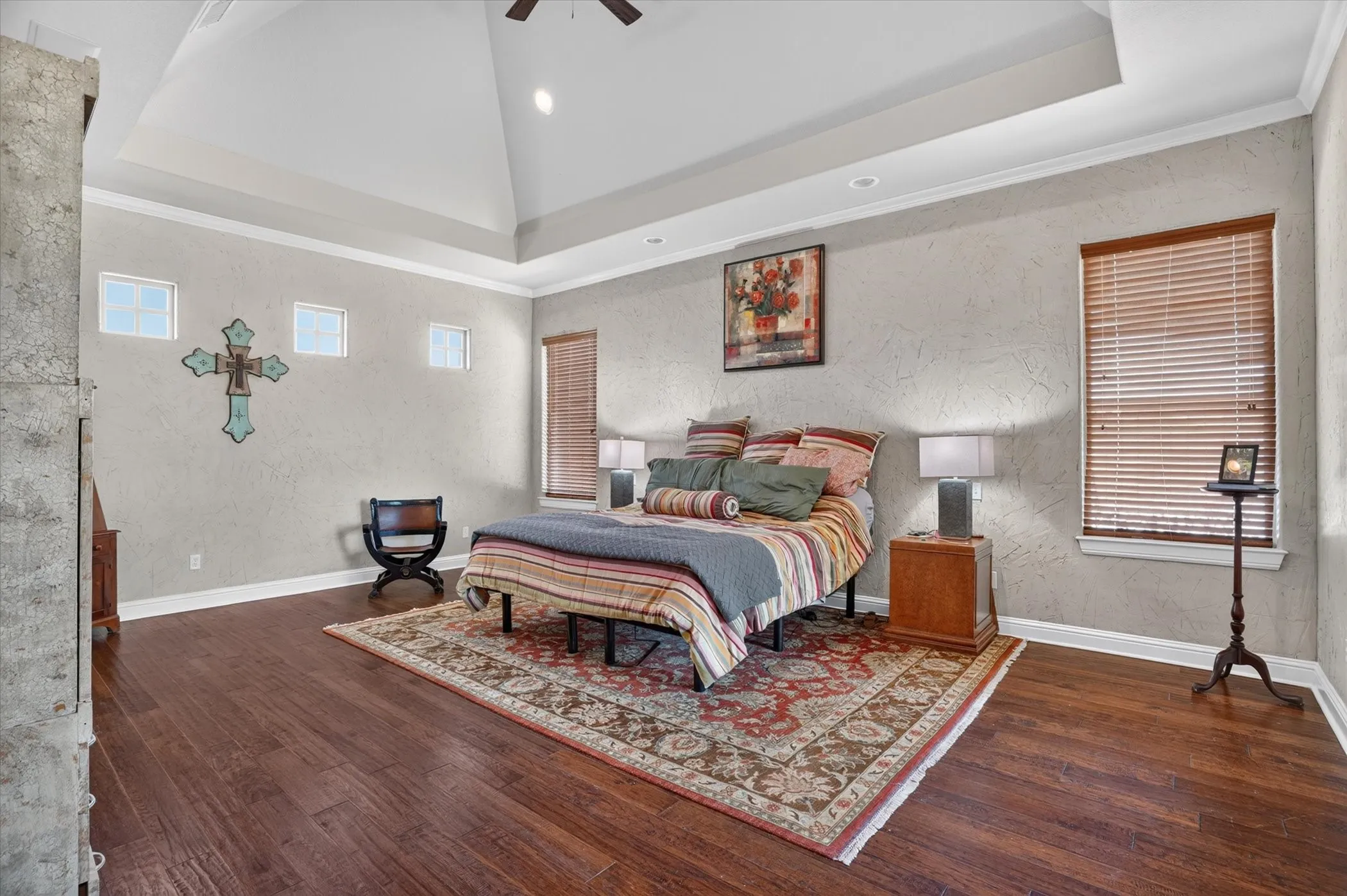 Spacious primary bedroom featuring a coffered ceiling with recessed lighting, hardwood flooring throughout, and large windows with wood-finish blinds