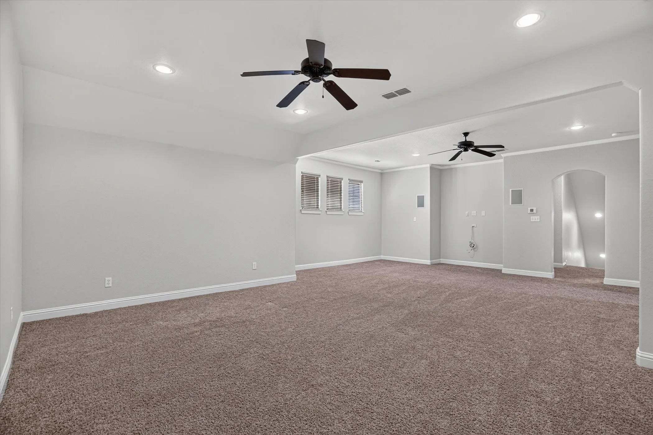 Expansive carpeted room featuring recessed lighting, multiple ceiling fans, and an arched entryway