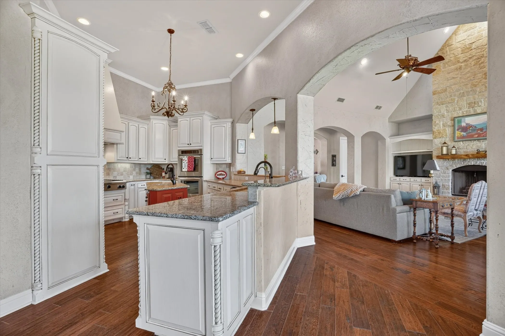Open-concept kitchen and living area featuring wood-finish flooring, white cabinetry, a kitchen island with a stone countertop, a stone-faced fireplace, and vaulted ceilings