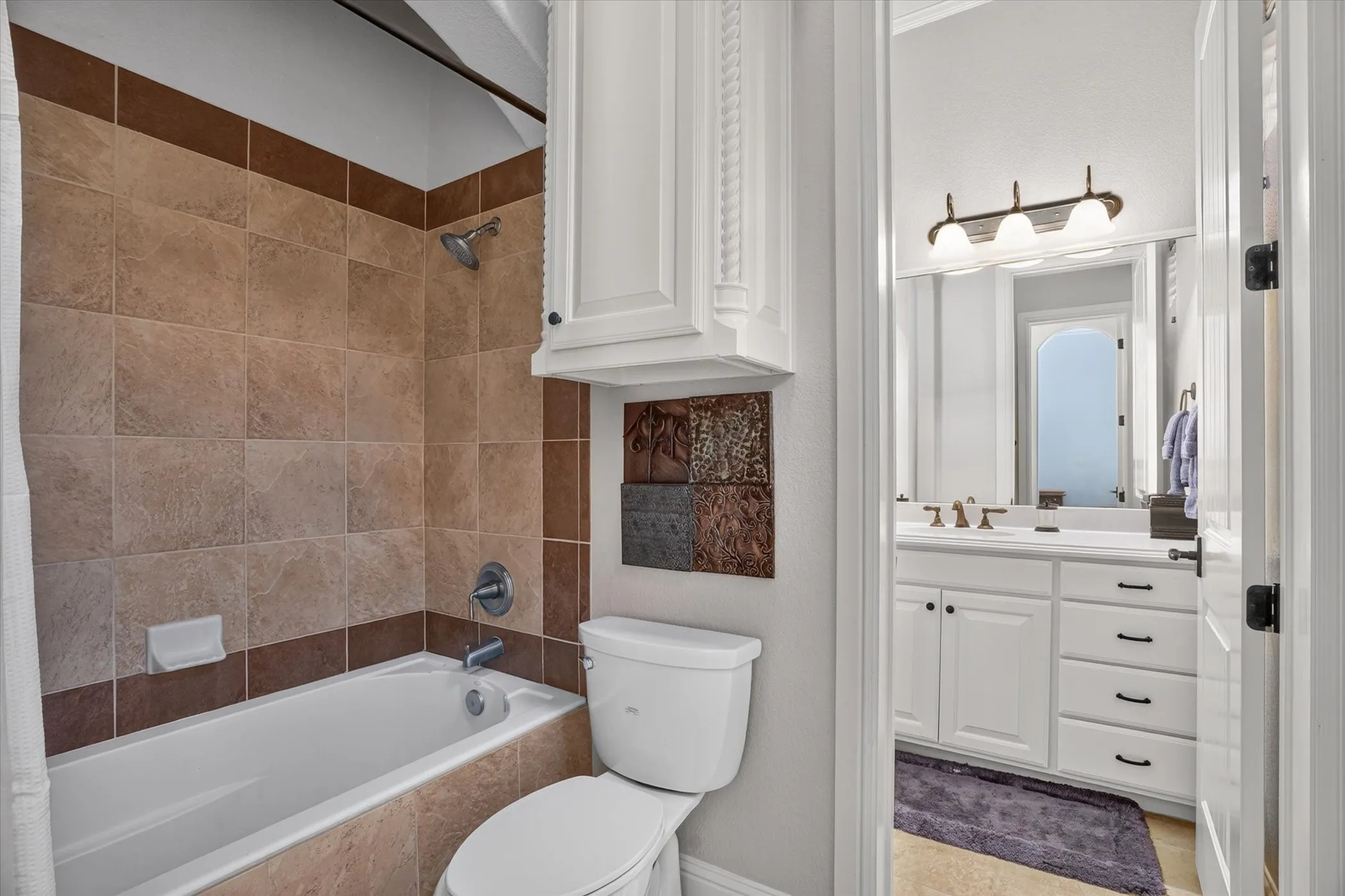 Spa-inspired bathroom featuring warm travertine tile surround, white cabinetry with brushed nickel hardware, and a vanity with integrated sink and countertop