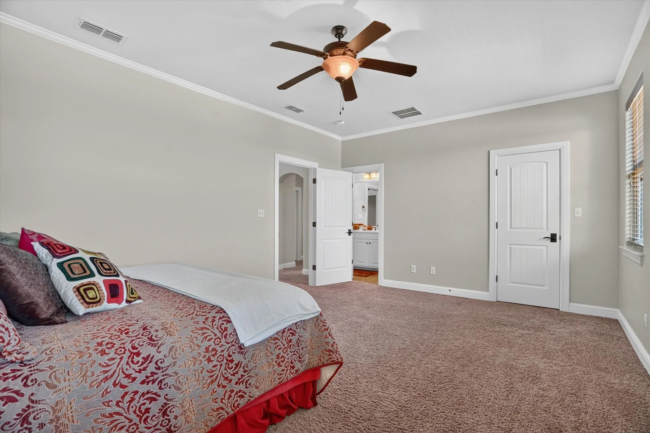 Spacious primary bedroom suite with ceiling fan, ensuite bathroom access, neutral wall finishes, and carpet flooring