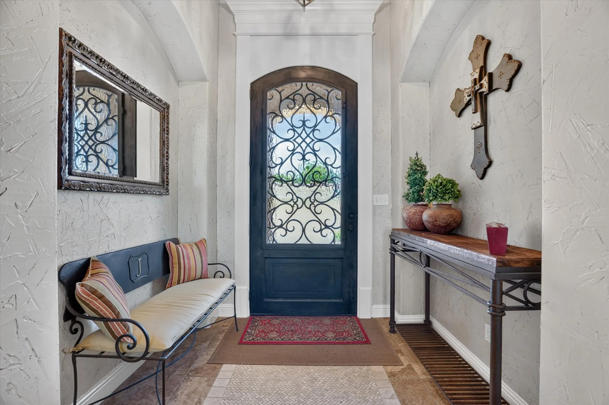 Elegant foyer showcasing white shiplap walls, decorative wrought-iron wall sconces, and a custom arched entry door with ornamental glass paneling