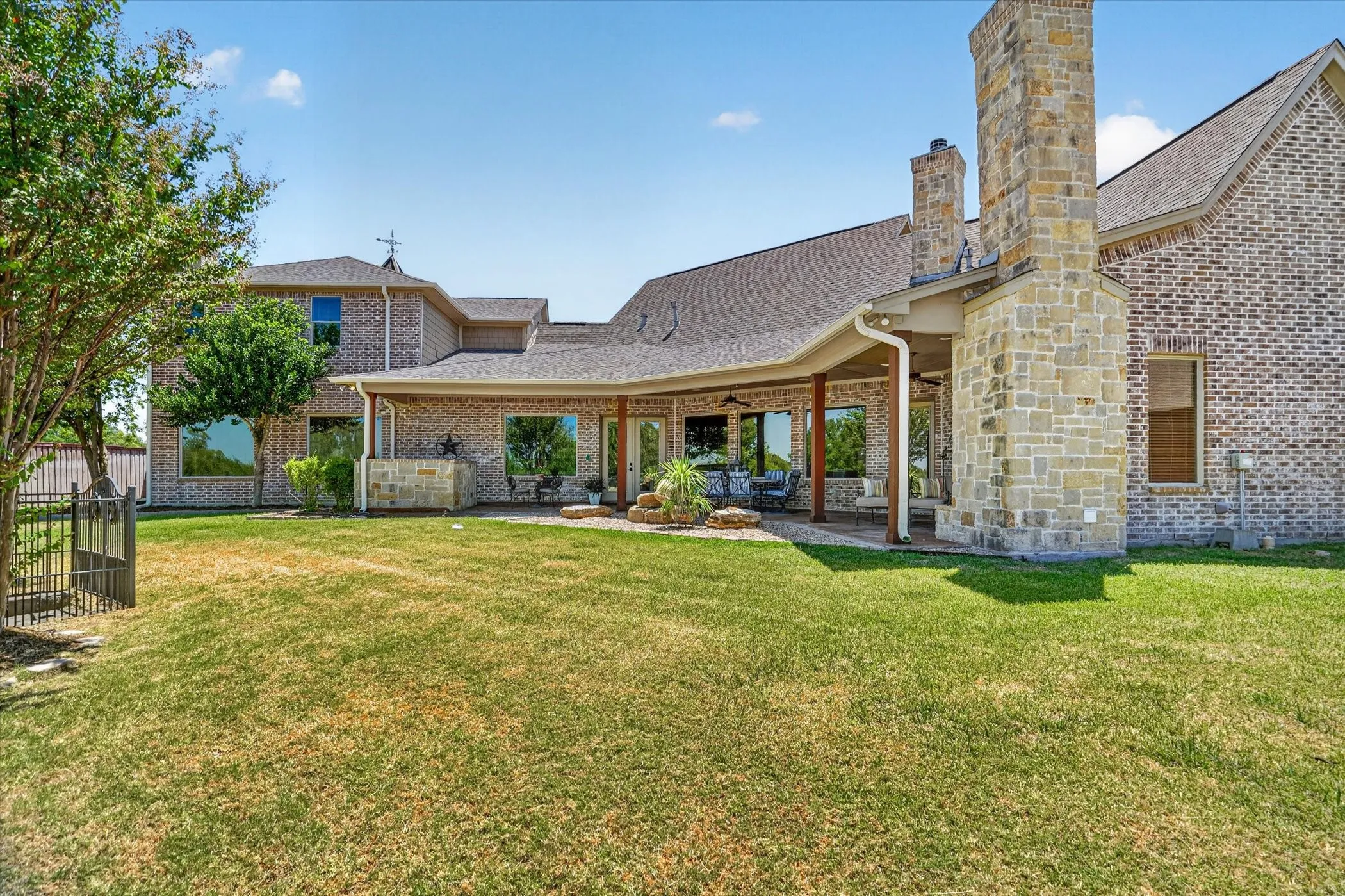 Brick and stone exterior with a covered patio, multiple large windows, and a shingle roof