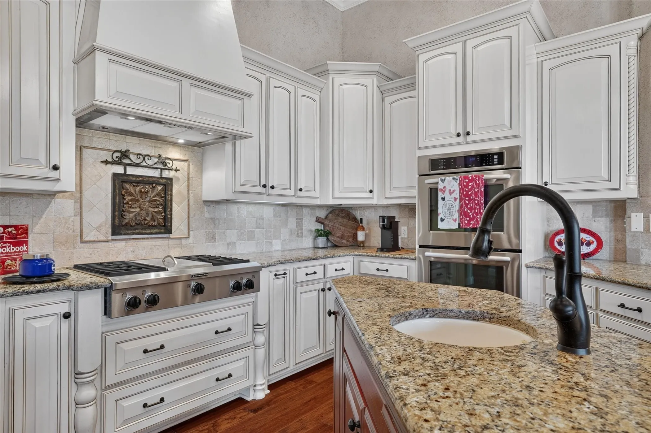 Chef's kitchen featuring white cabinetry with detailed paneling, granite countertops, and a large center island with undermount sink and matte black faucet