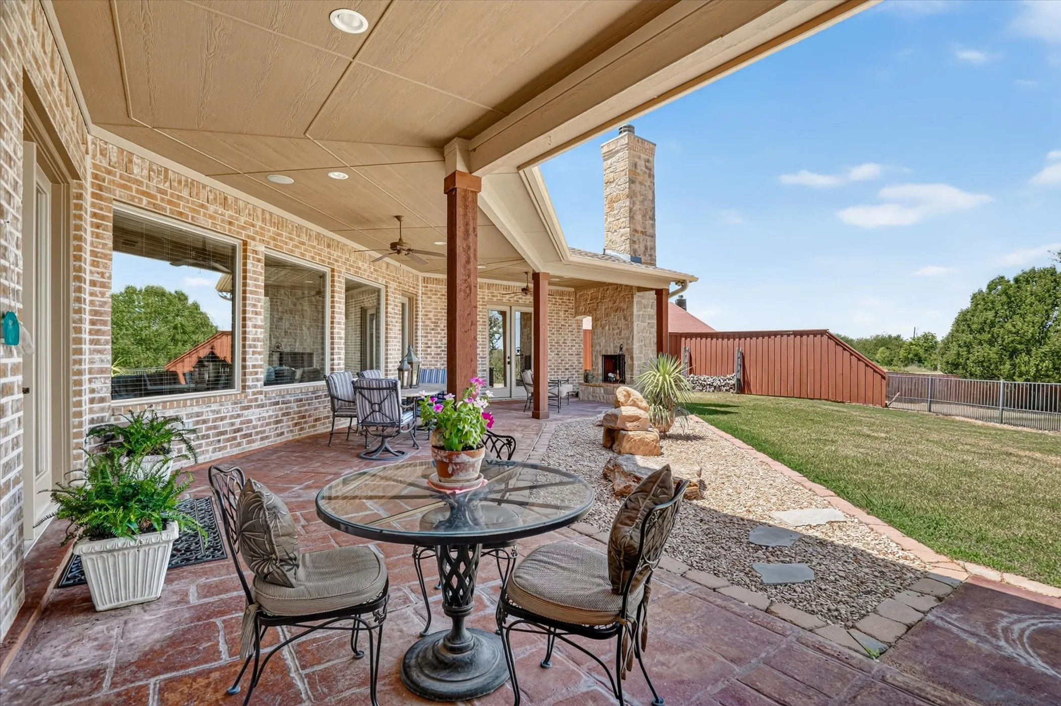 Expansive covered patio with brick and stone accents, ceiling fans, recessed lighting, and a built-in outdoor fireplace