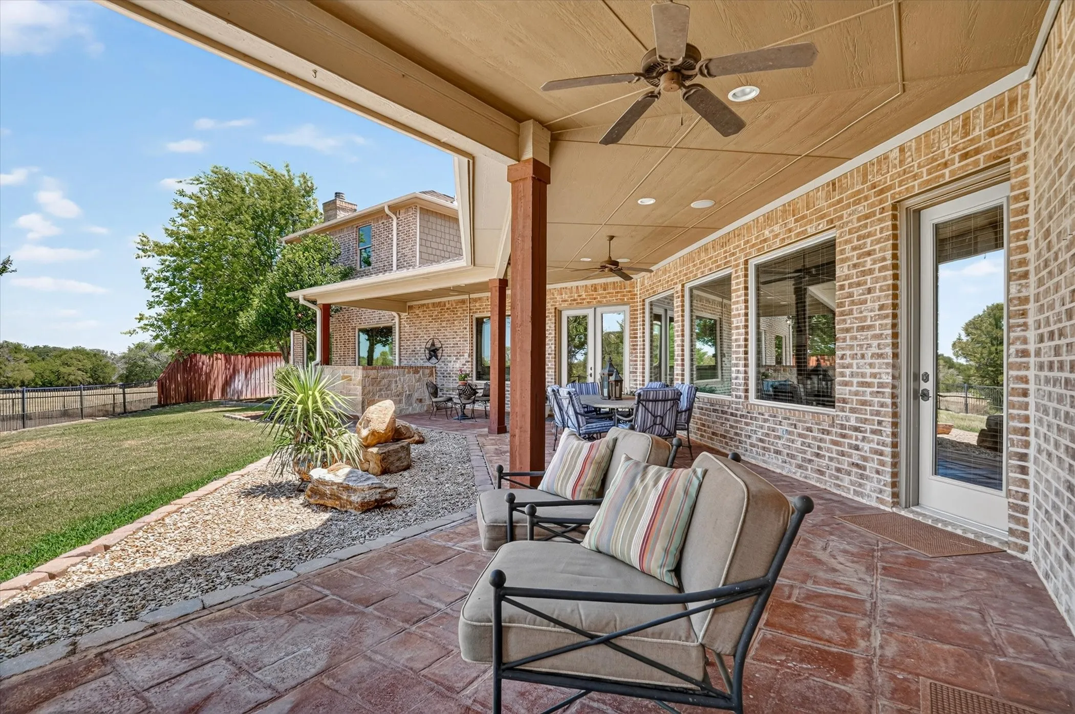 Expansive covered patio featuring stamped concrete flooring, brick exterior, multiple ceiling fans, recessed lighting, and large windows