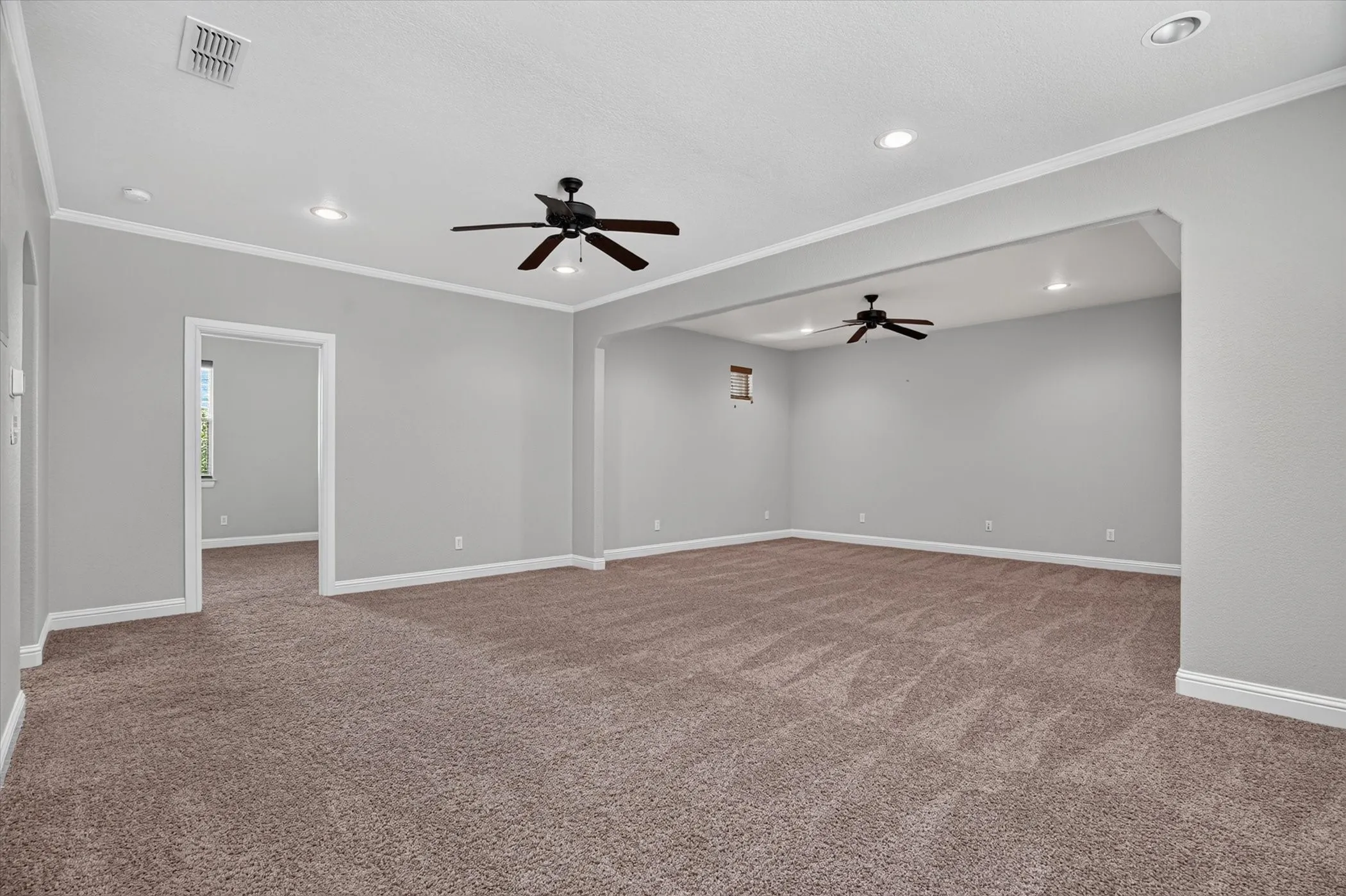 Expansive carpeted room with multiple recessed lights and two ceiling fans