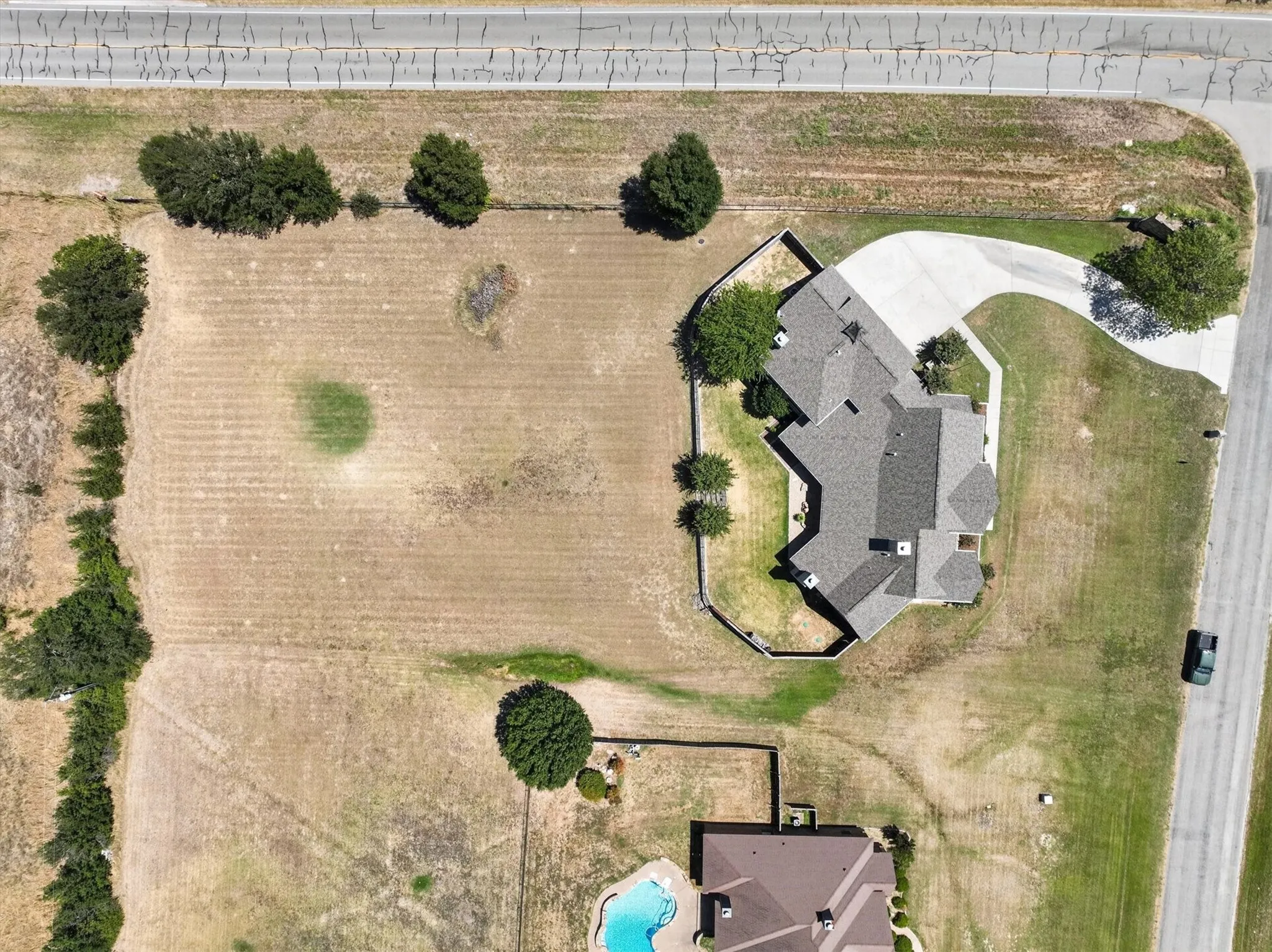 Expansive lot featuring a main residence with a multi-gabled roof, an extended paved driveway, and mature landscaping