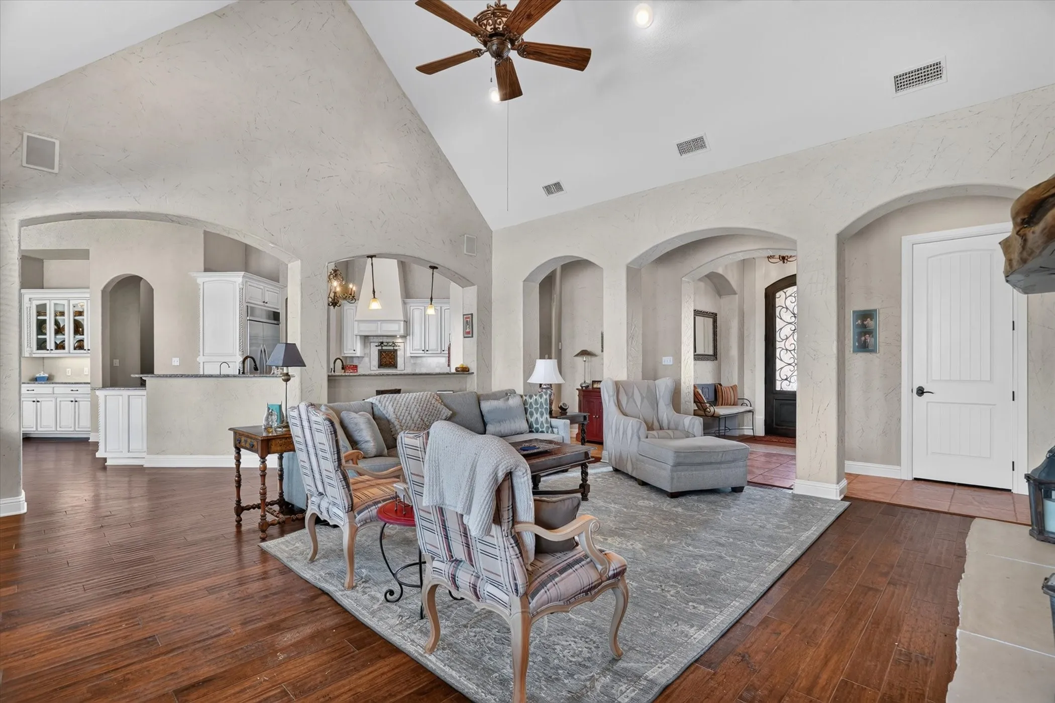 Vaulted ceiling with a wood-finish ceiling fan, wood-finish flooring, and arched doorways
