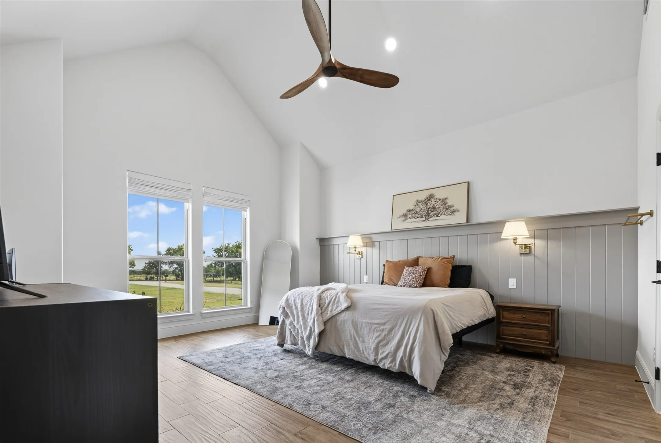 Primary bedroom suite featuring vaulted ceilings with ceiling fan, wood-finish flooring, and expansive glass doors opening to outdoor landscape