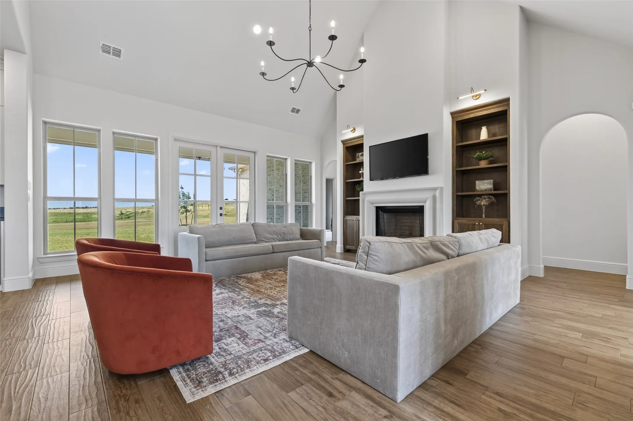 Vaulted ceiling with an exposed beam, fireplace with a mantel, built-in shelving, glass-paneled doors, and wood-finish flooring